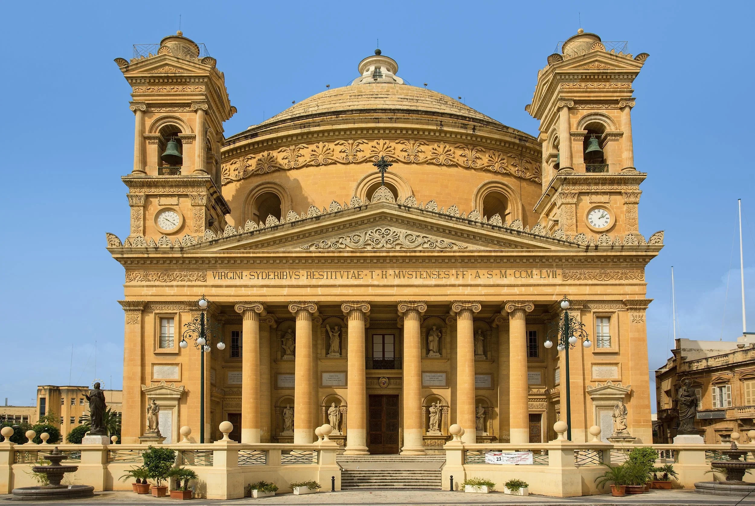 Mosta Dome with large ornate columns, statues, and a domed roof, under a clear blue sky.