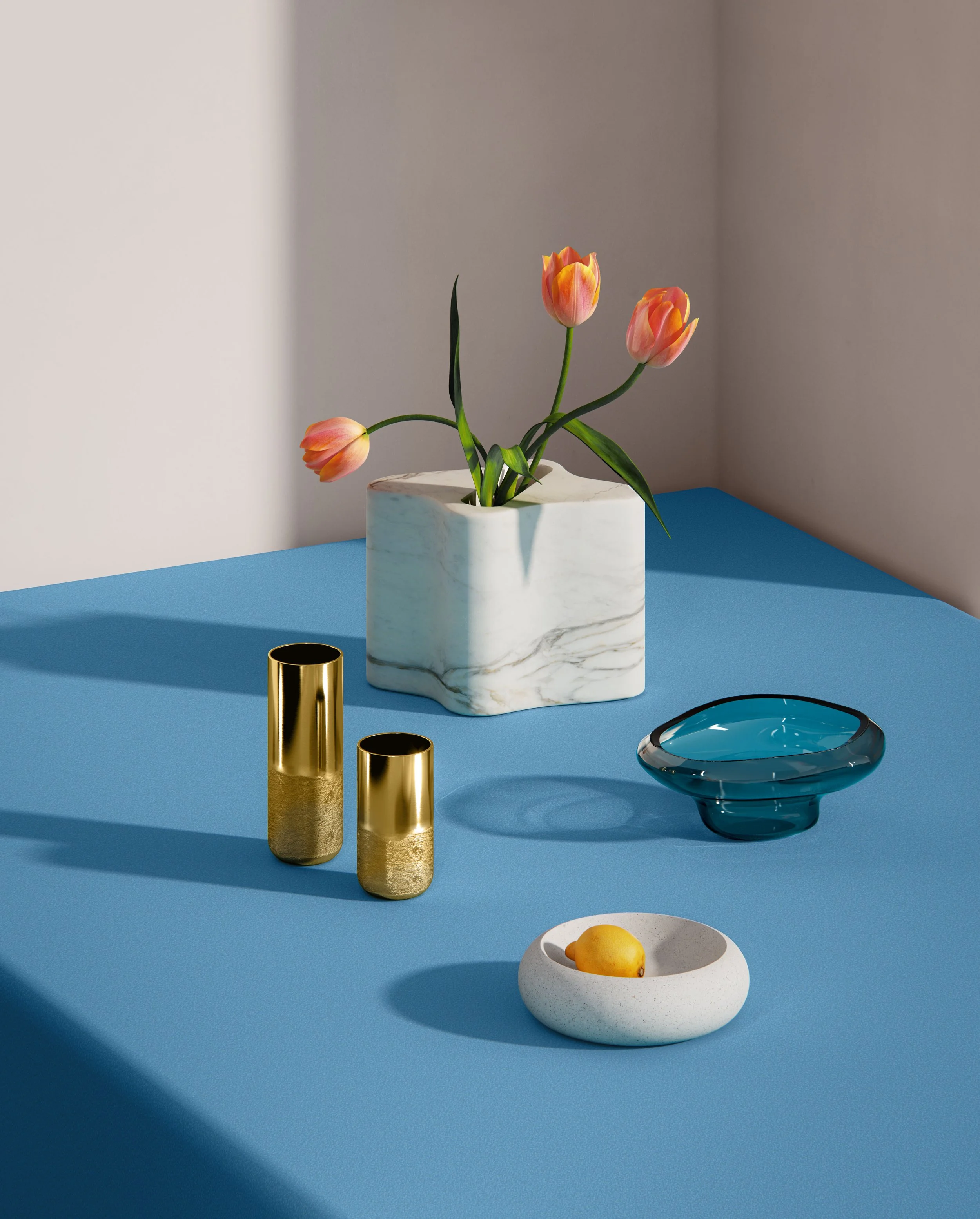A white marble square vase with pink tulips on a blue tabletop, a blue glass bowl, and a white bowl with a lemon.