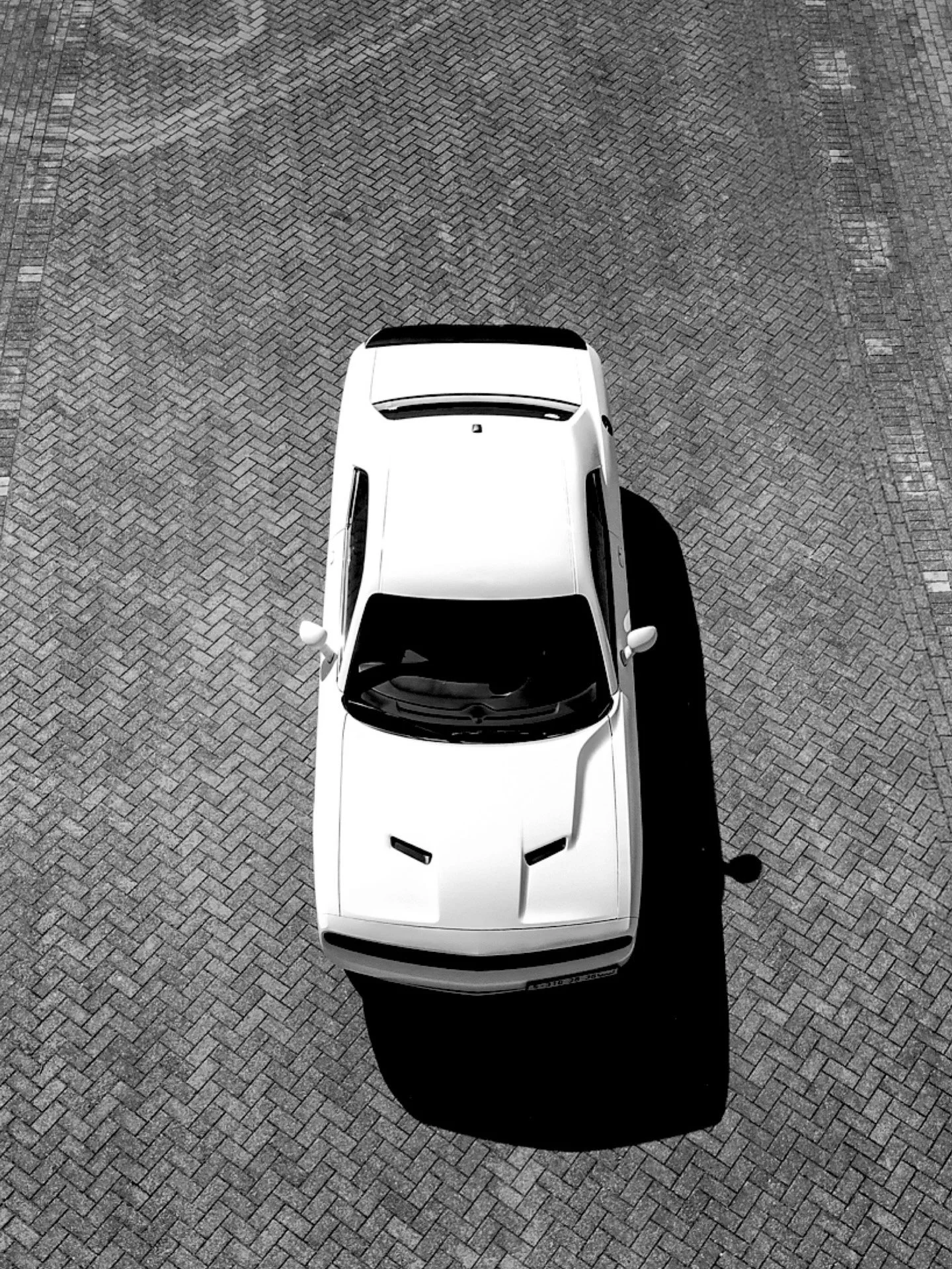 Top-down view of a white car parked on a patterned brick surface.