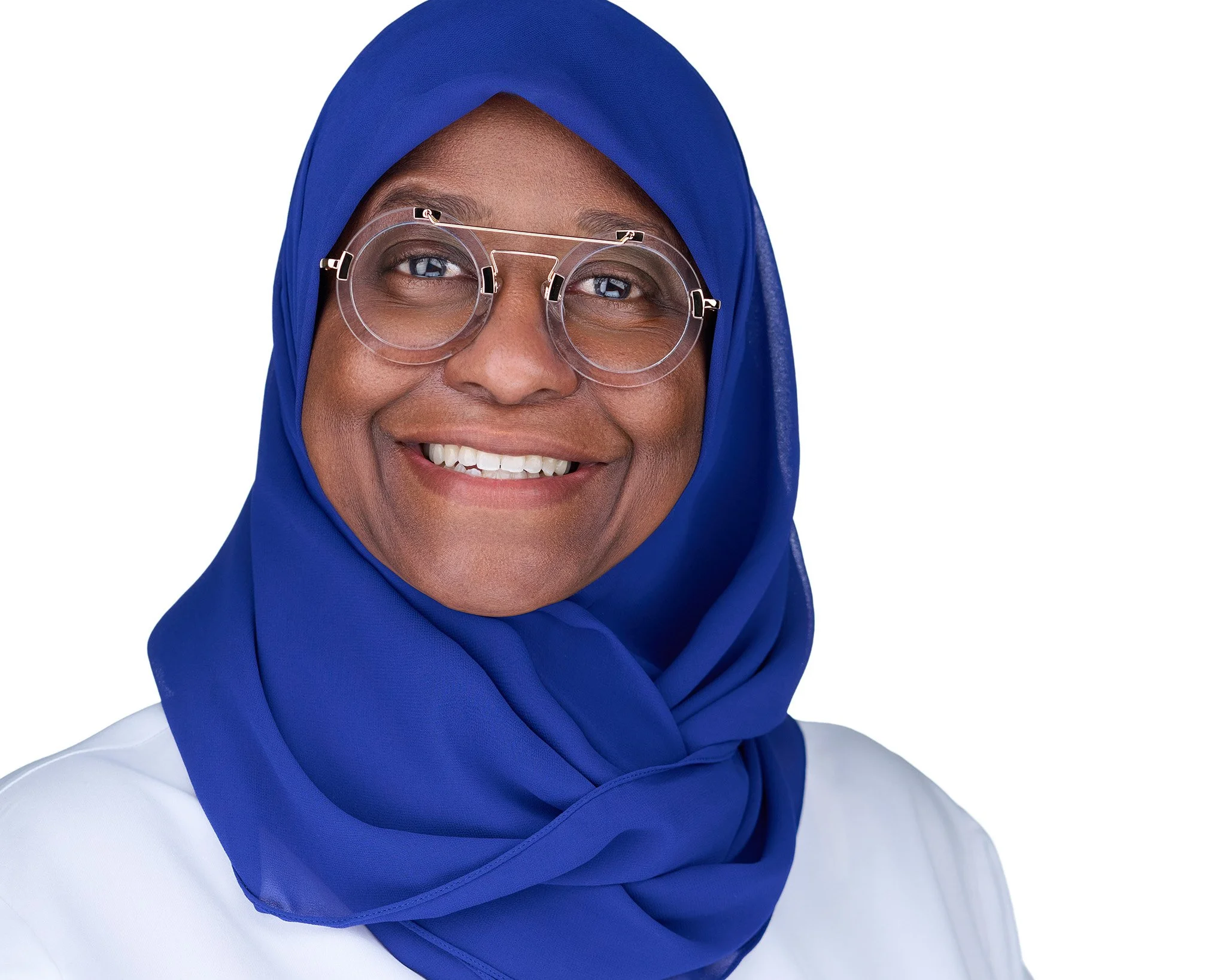 Close-up of a smiling woman wearing a blue hijab and clear round glasses, against a plain white background.