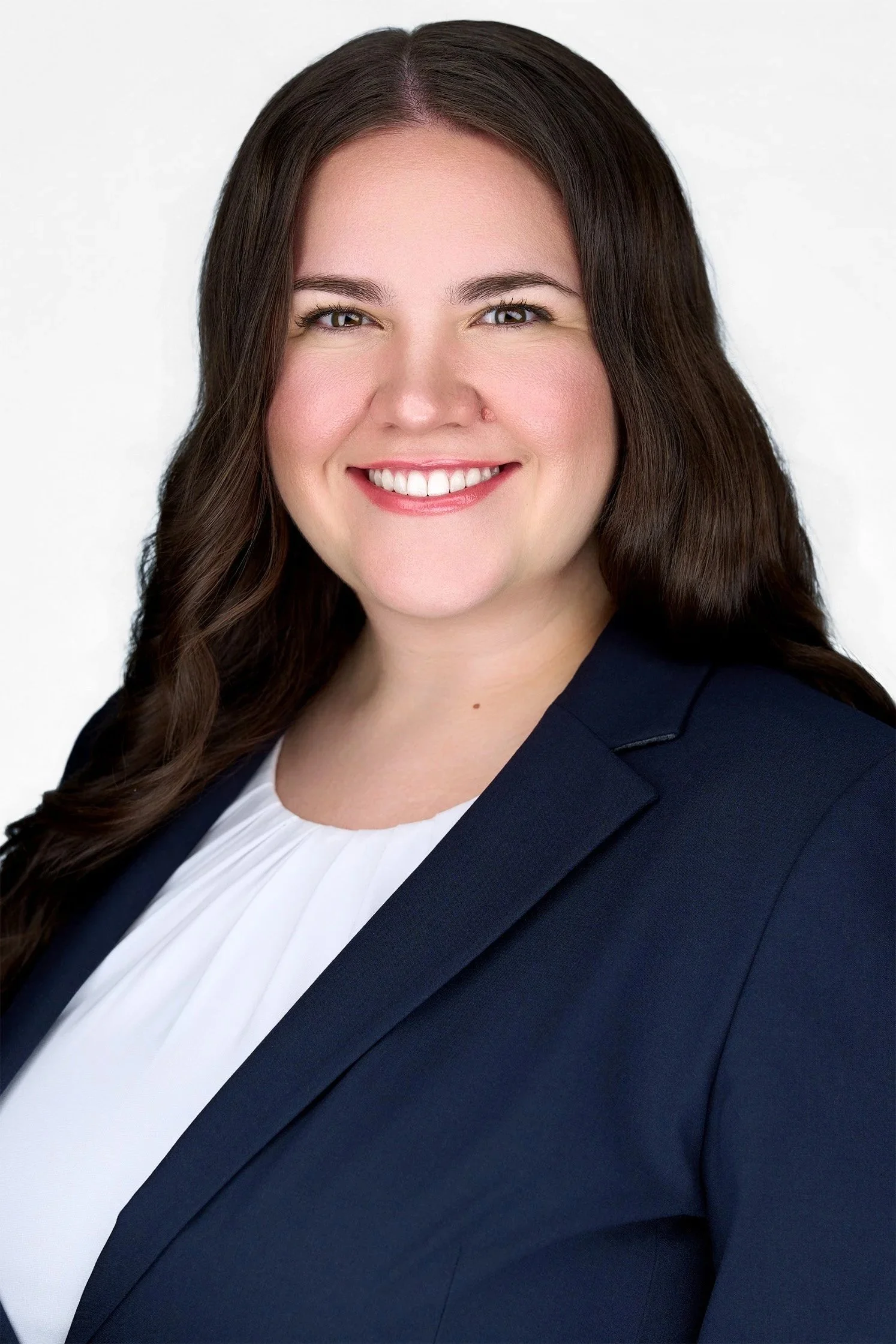 Woman with long brown hair, in a navy blazer and white blouse, smiling for her ERAS headshot against a white background.