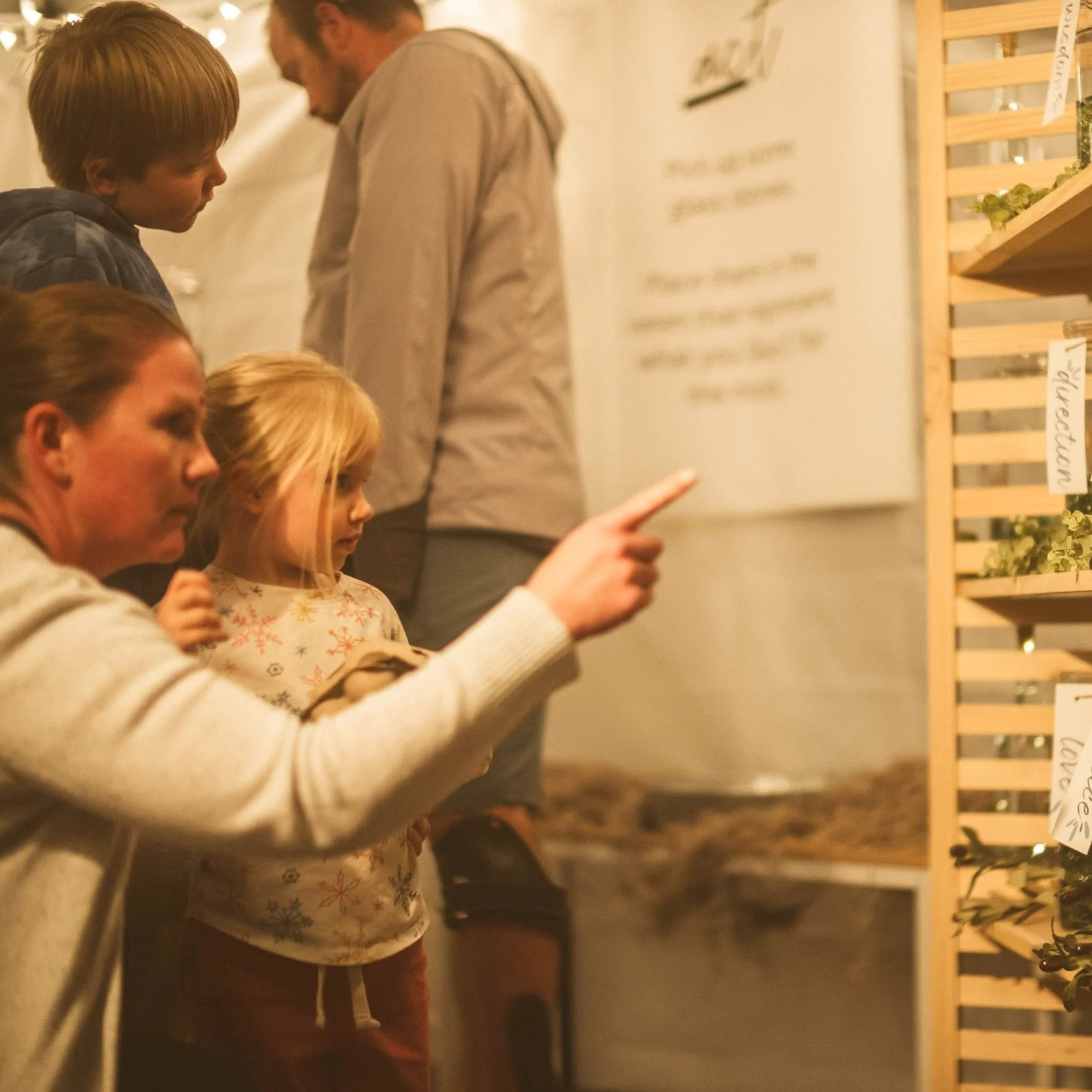 A woman and a young girl looking and pointing at a display of plants at an indoor market.