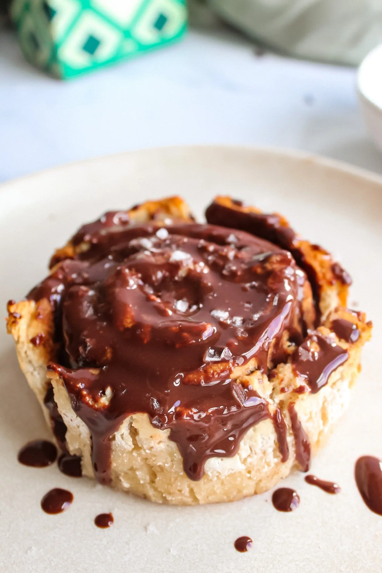 A cinnamon roll topped with chocolate glaze on a white plate.