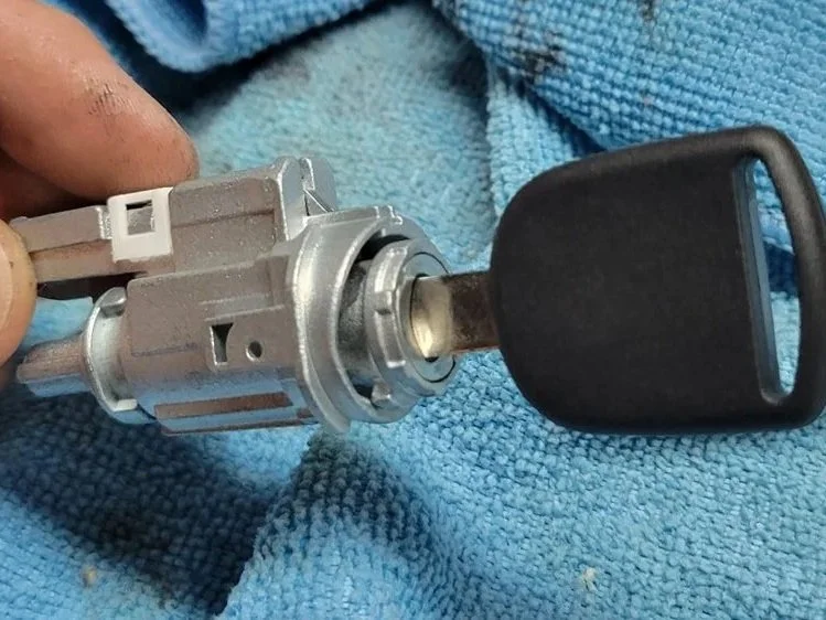 Close-up of a car ignition switch with a key inserted, lying on a blue textured cloth.