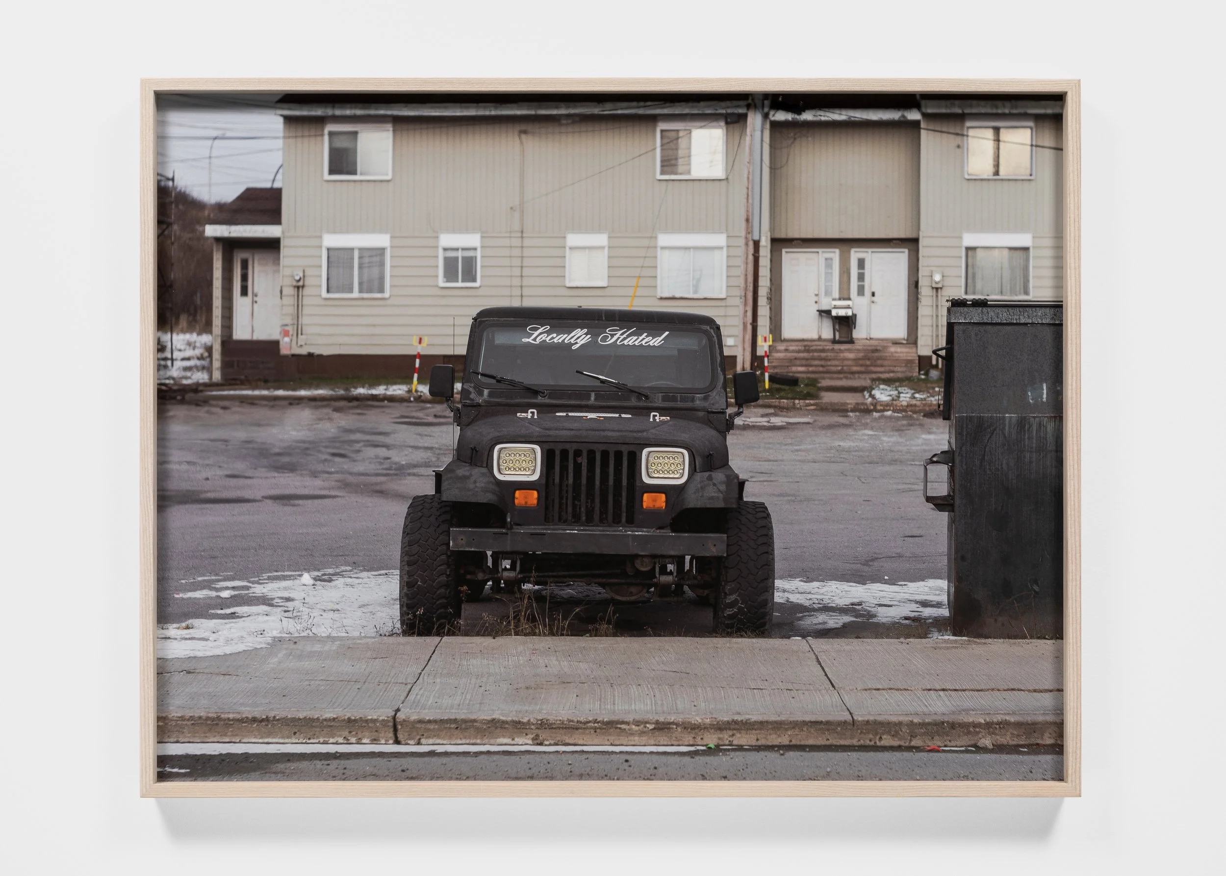 Black off-road vehicle parked on a street, partially covered in snow, with a building in the background.