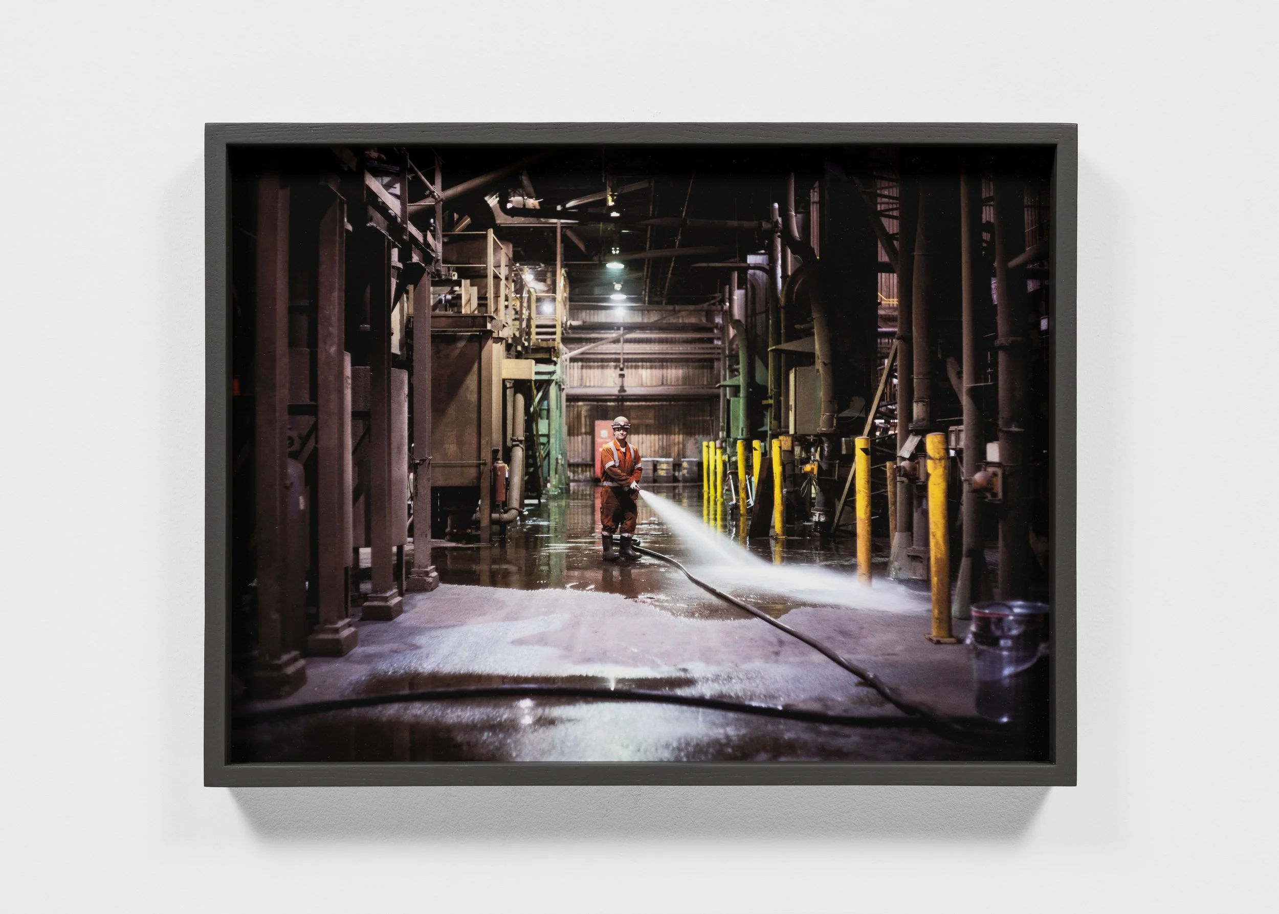 Person using a hose to clean a wet industrial facility with equipment and yellow guardrails.