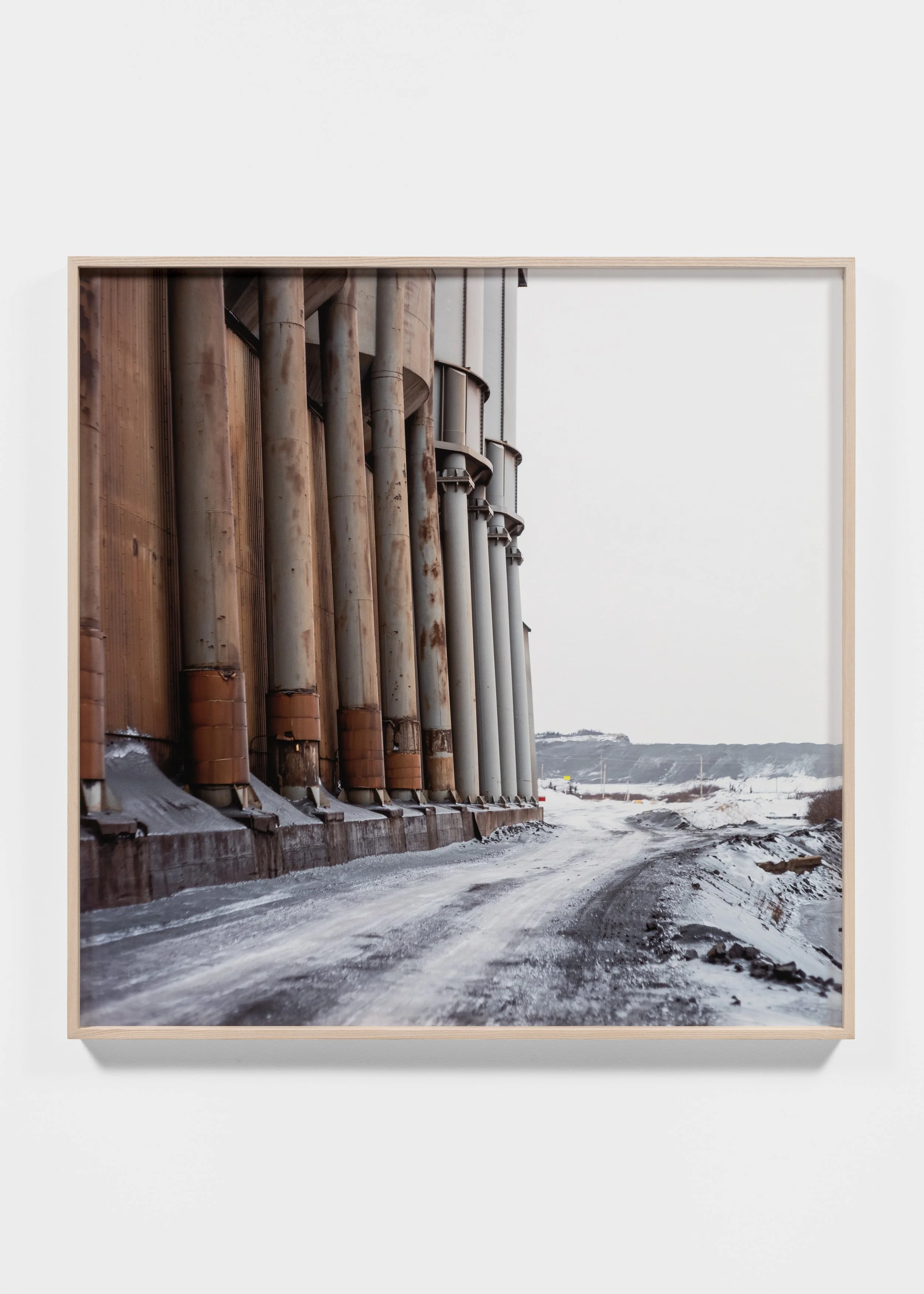 Industrial structure with large vertical metal pipes along a snowy, dirt road.