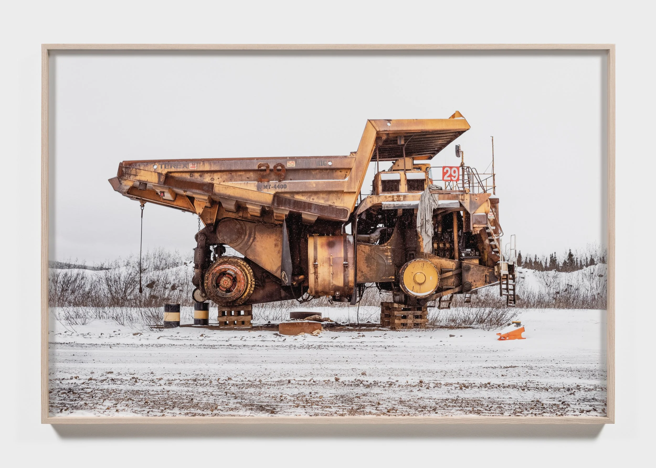 A large, partially disassembled mining truck on a snowy landscape, elevated on blocks with missing wheels and components.