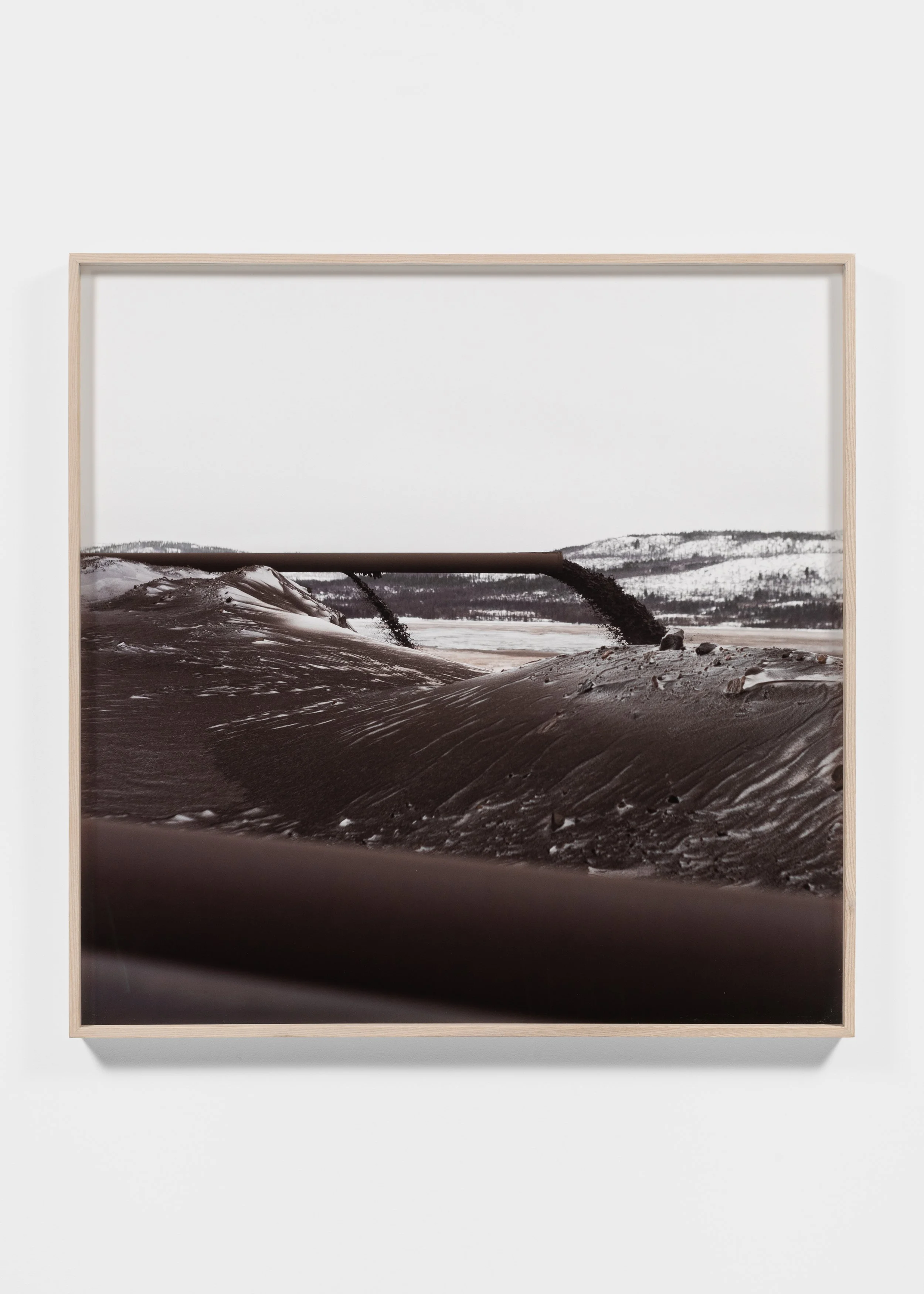 Framed photograph of a snowy mountain landscape with dark, flowing liquid and pipes.
