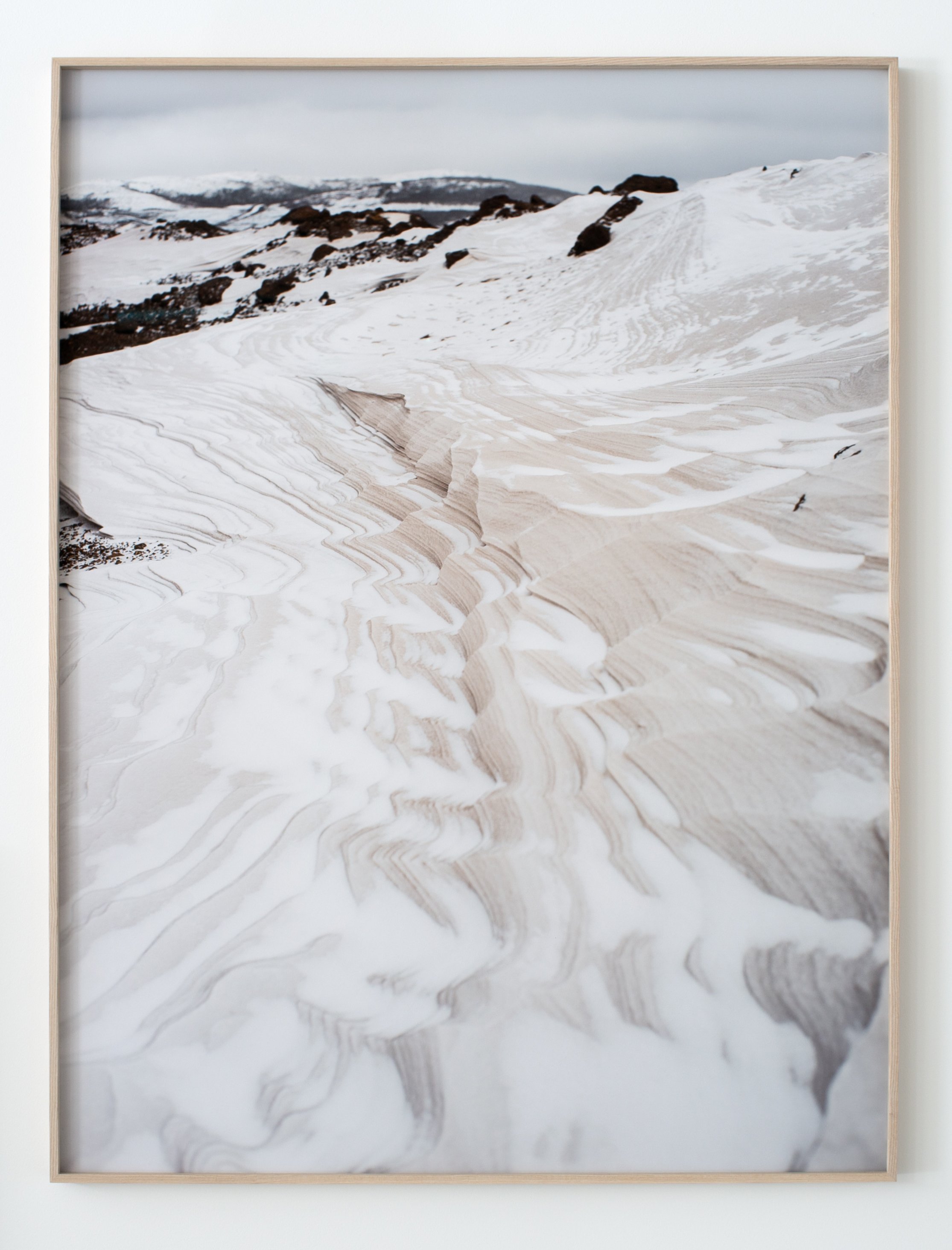 Snow-covered landscape with sand-like textures and scattered rocks under a cloudy sky.