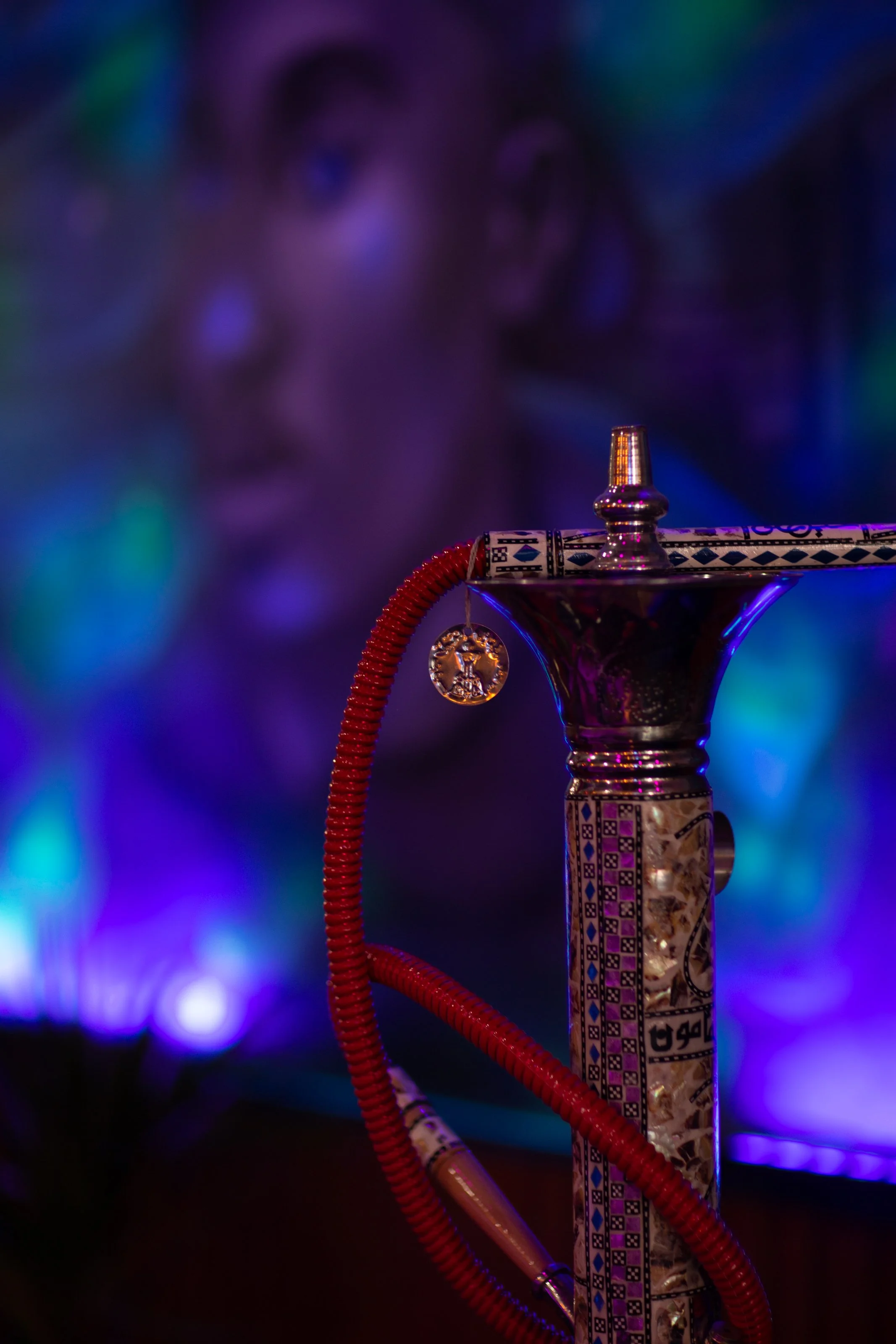 Close-up of a decorative hookah with a red hose and intricate patterns against a colorful blurred background.