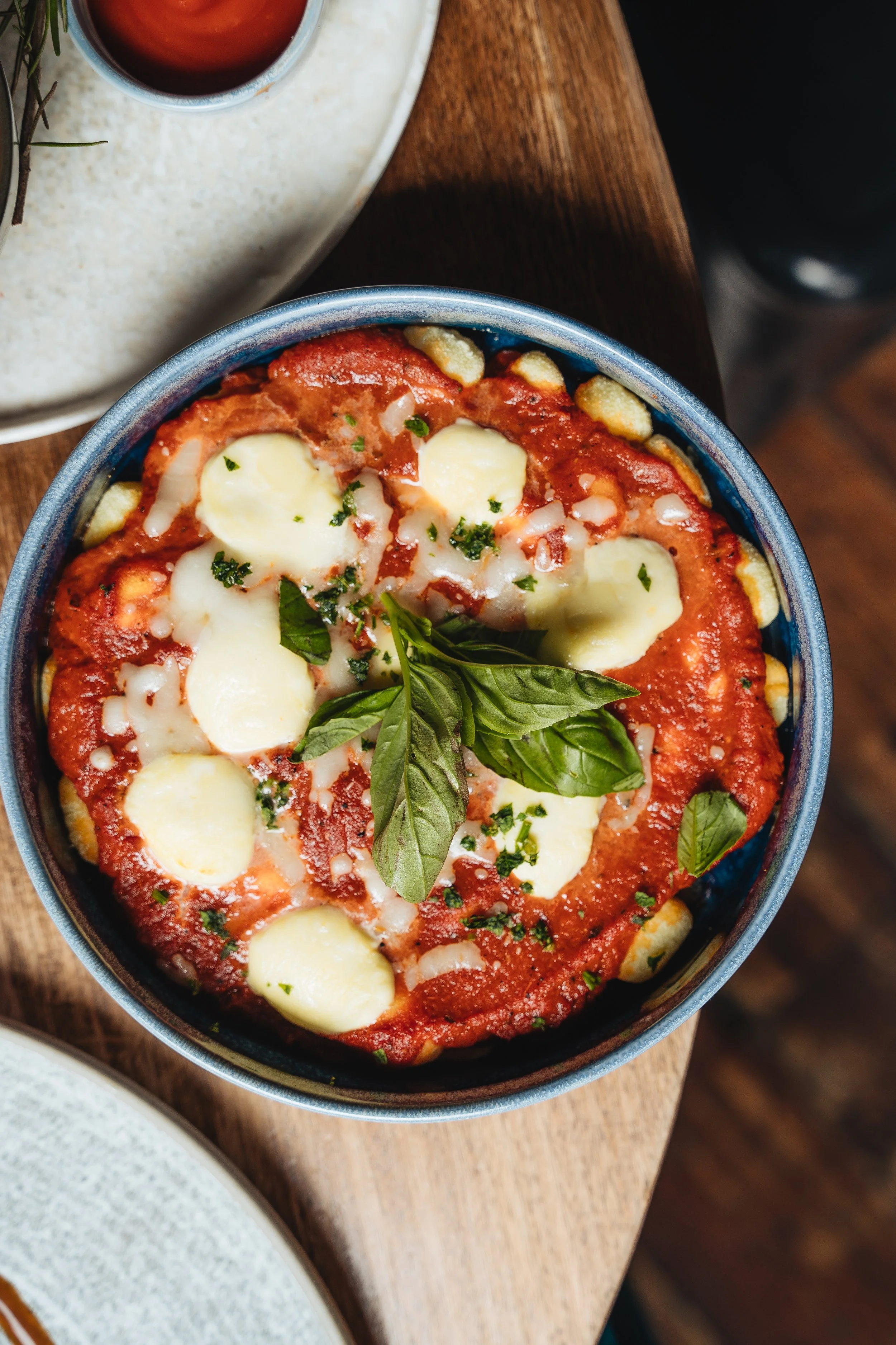 Gnocchi with tomato sauce, cheese, and basil leaves in a blue bowl.
