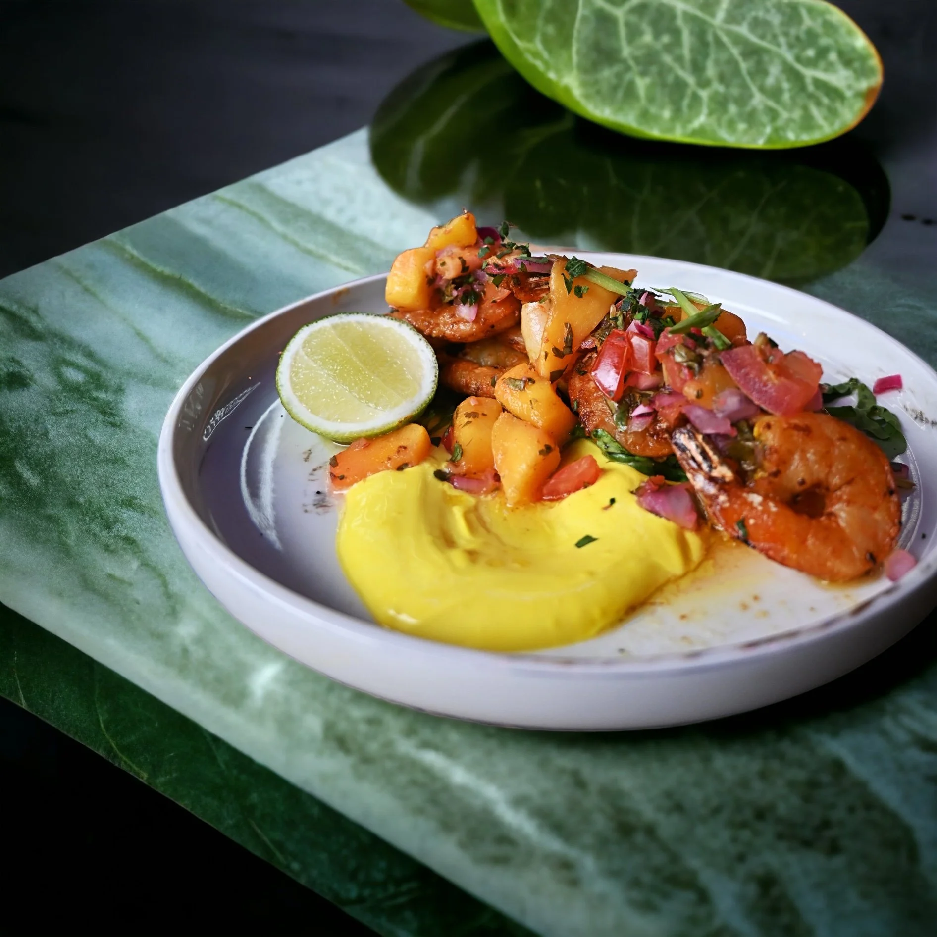Plate of grilled shrimp with mango salsa, lime wedge, and yellow sauce on green surface.