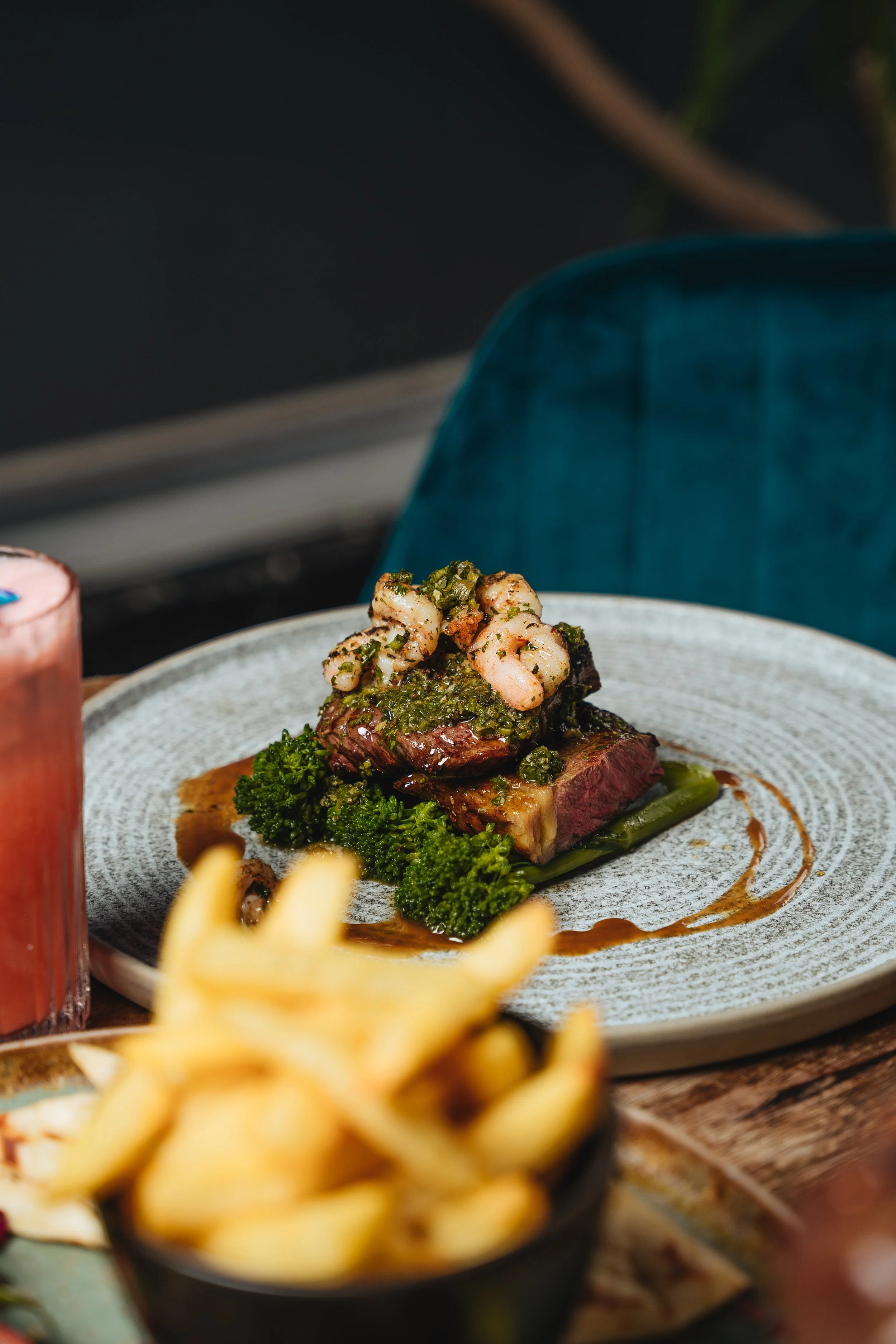 Plate of steak topped with shrimp and greens, accompanied by a side of fries and a drink.