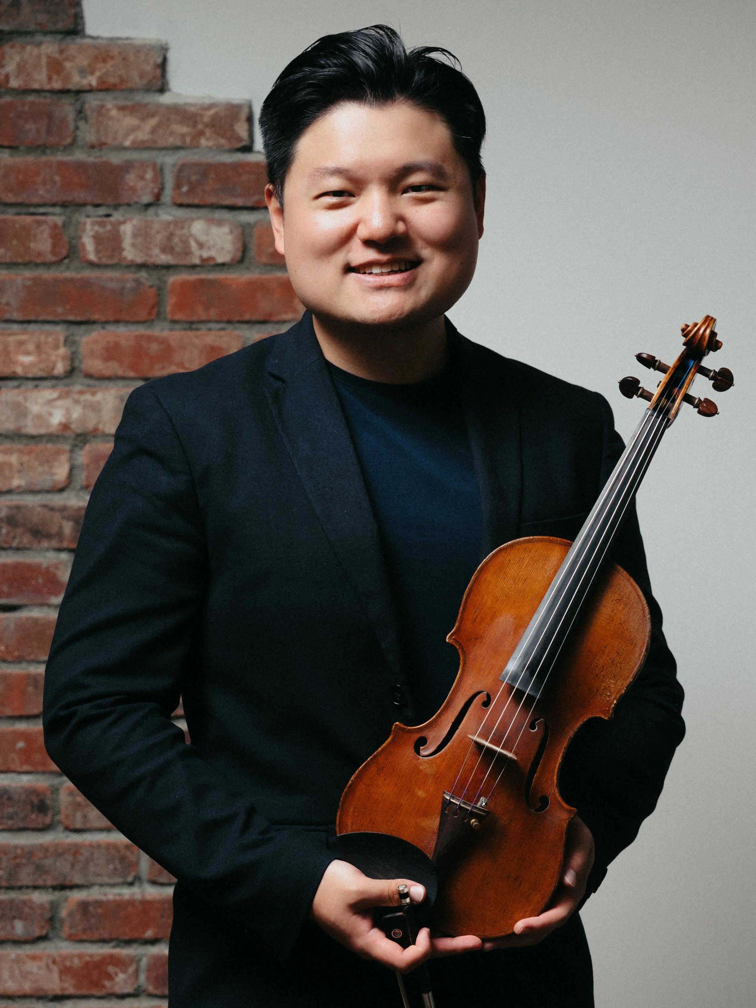 A man standing in front of a stone wall holding a violin and a bow