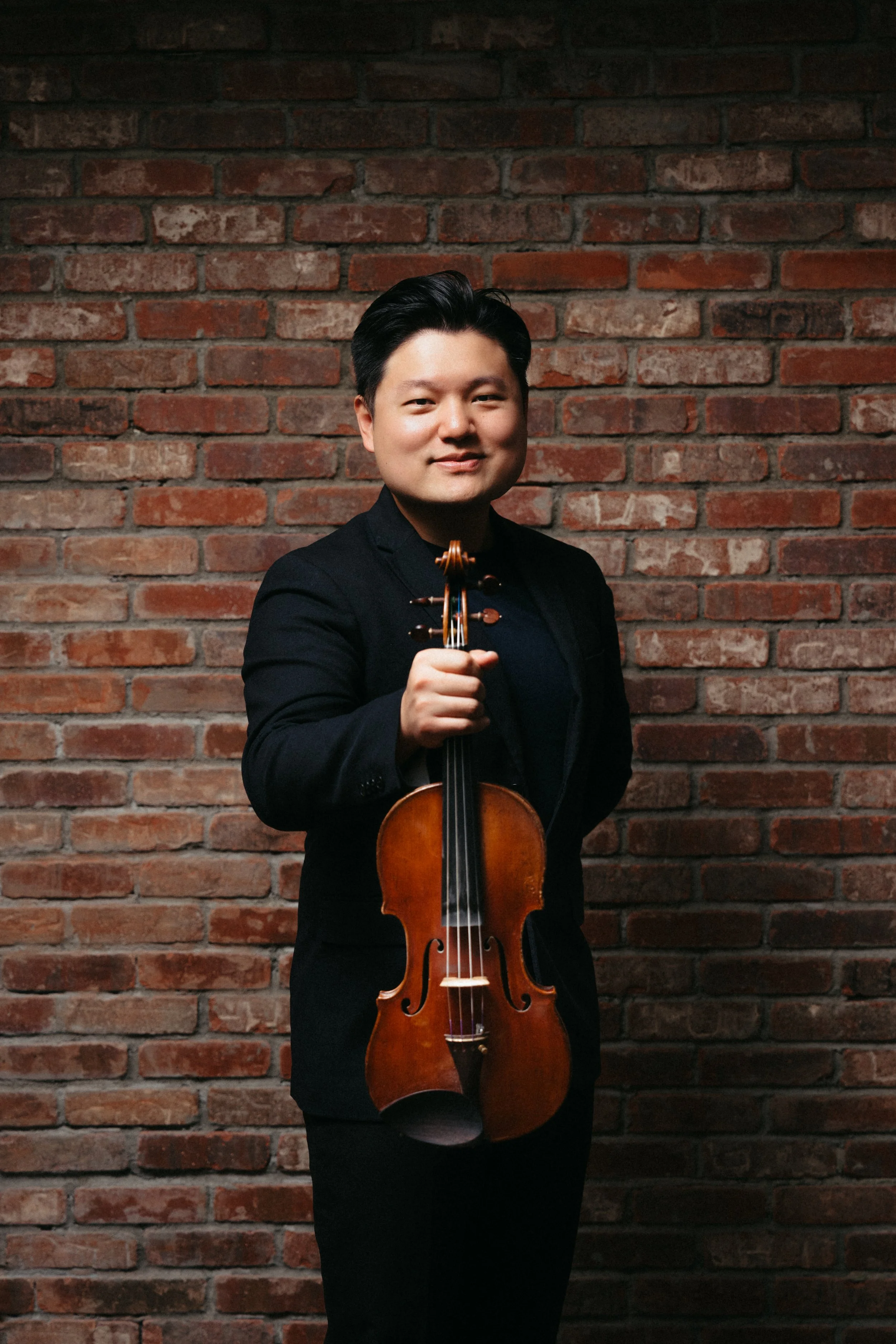 A man standing in front of a stone wall holding a violin and a bow