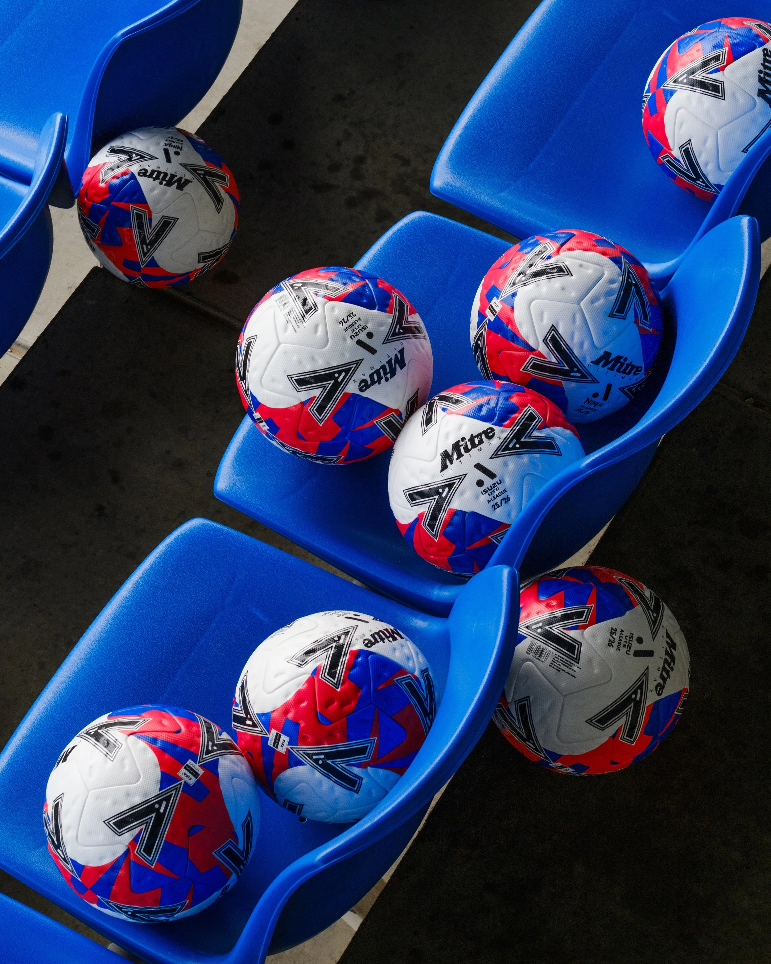 Baseballs with colorful red, white, and blue designs resting on blue stadium seats.