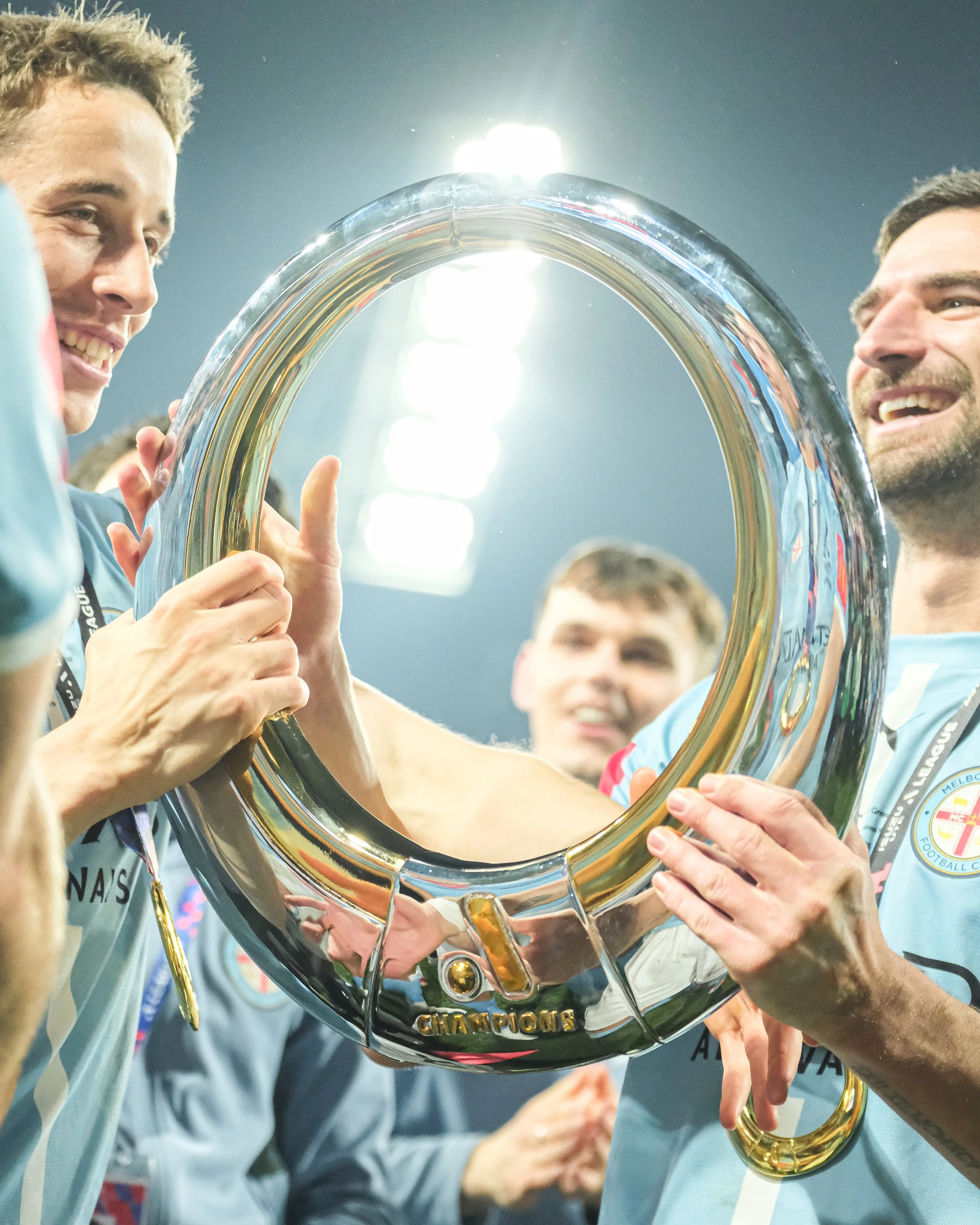 Two people holding a shiny championship trophy, smiling and celebrating.