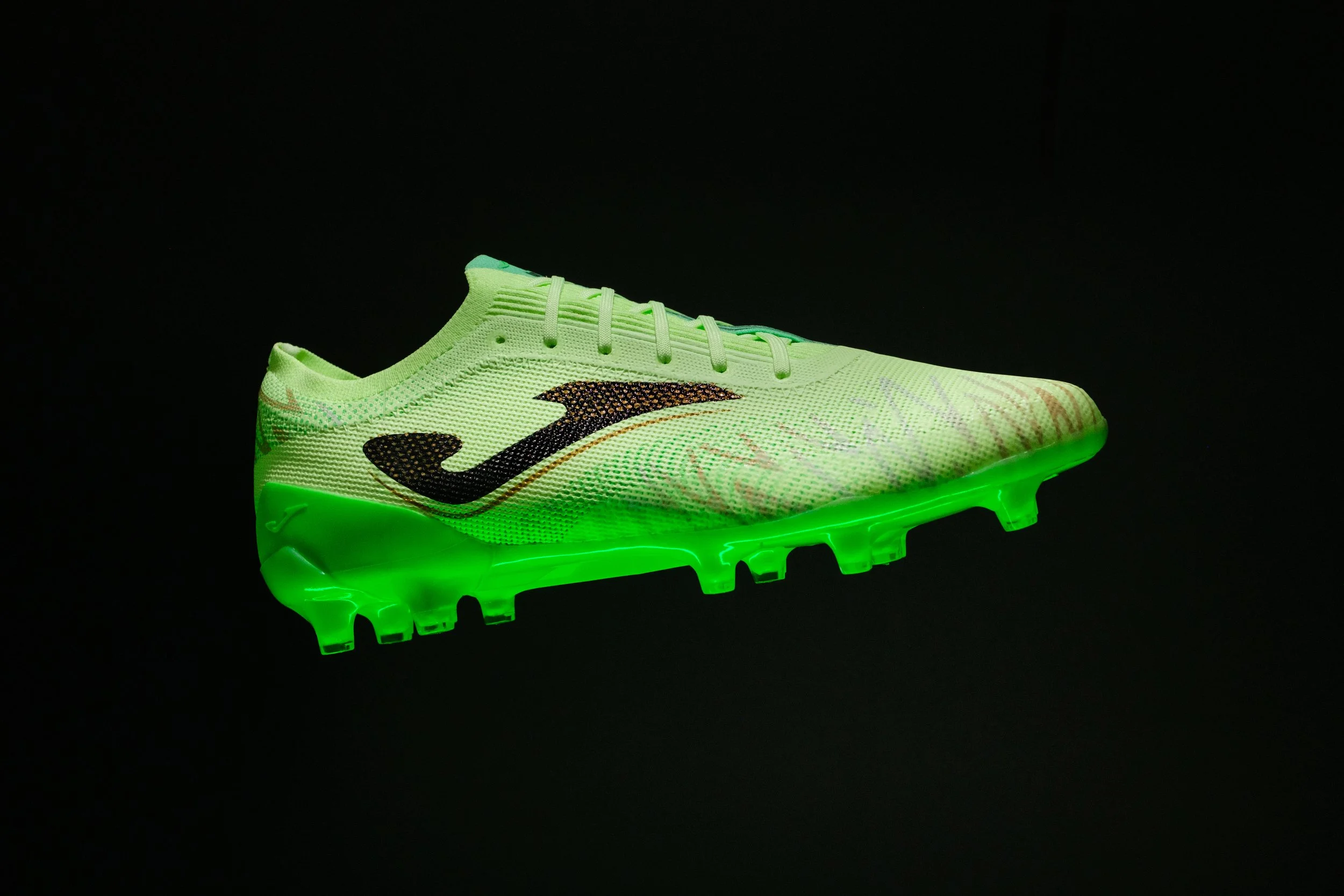 A glowing green and black athletic shoe with a patterned design, illuminated against a black background.
