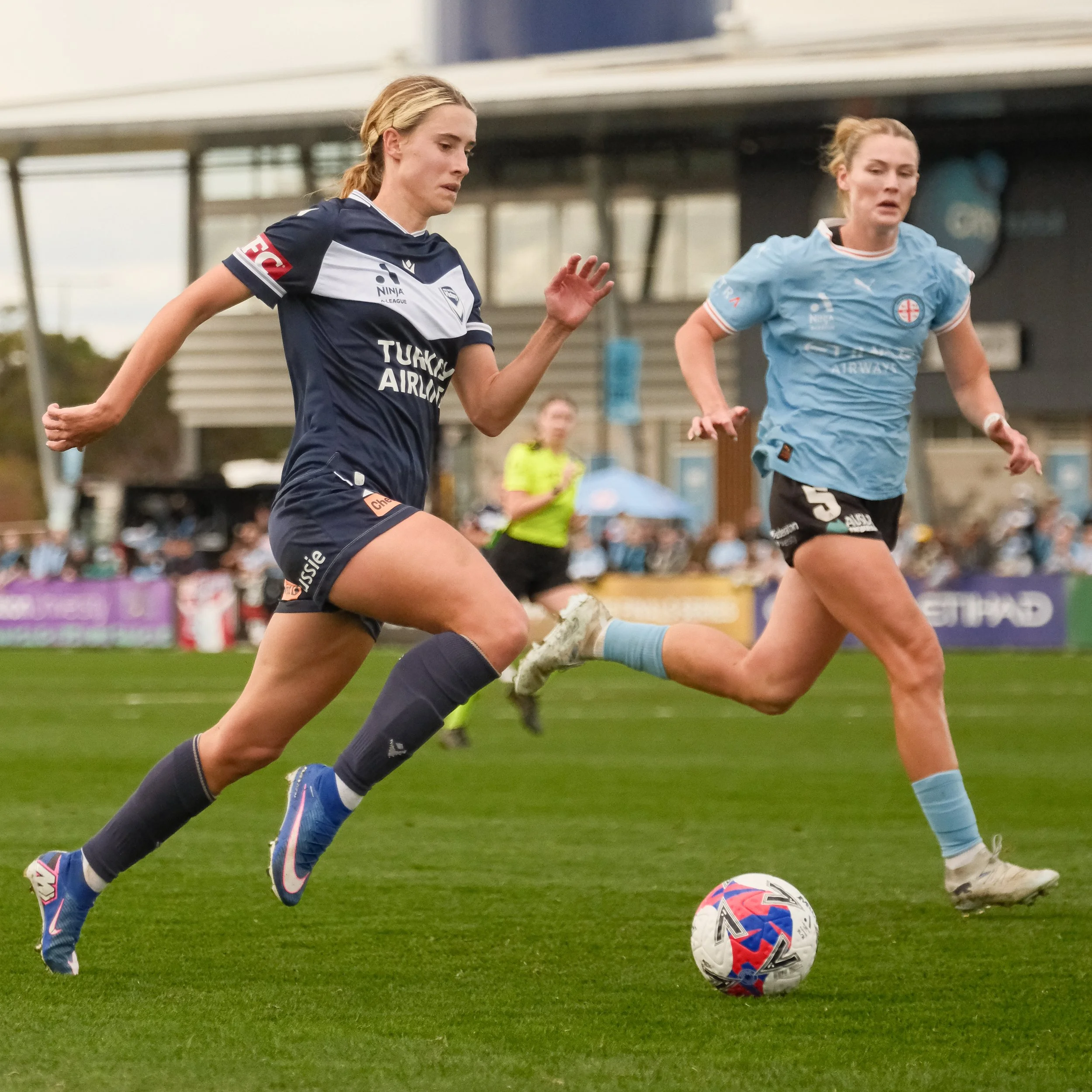 Women in soccer uniforms running on a field chasing a soccer ball.