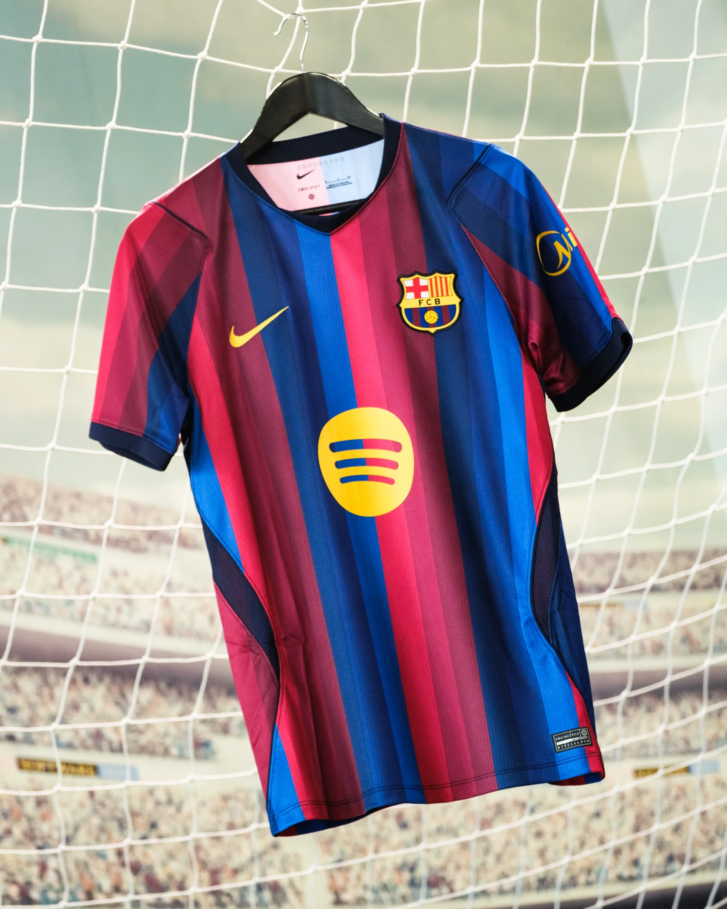 A soccer jersey with red and blue vertical stripes hanging on a hanger in front of a soccer goal net.