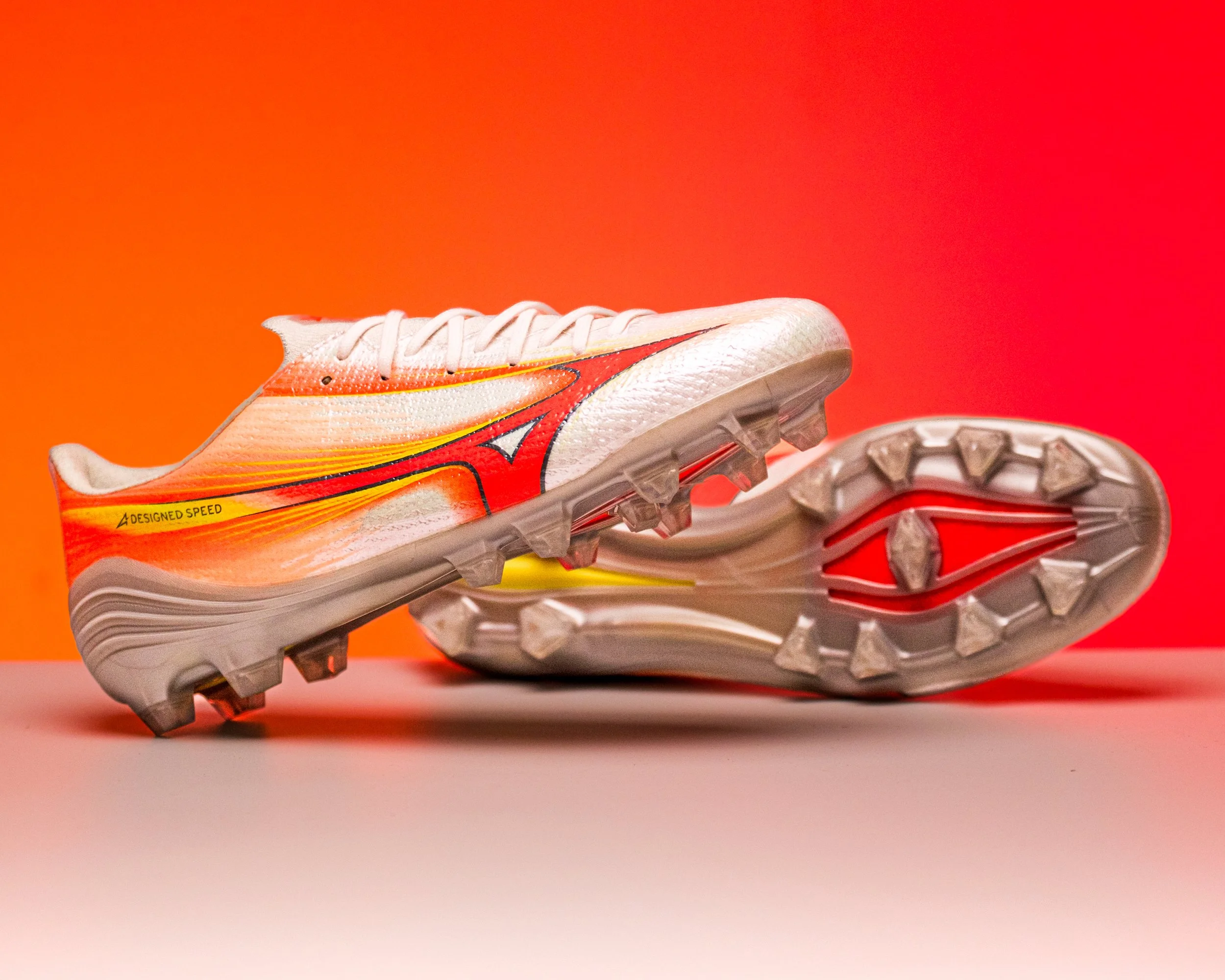 A close-up of a running shoe with a red and yellow design, placed on a pink and red background.