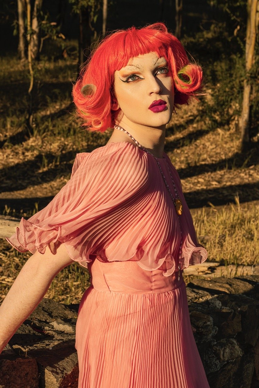 Person in a pink pleated dress with bright red hair in an outdoor setting.