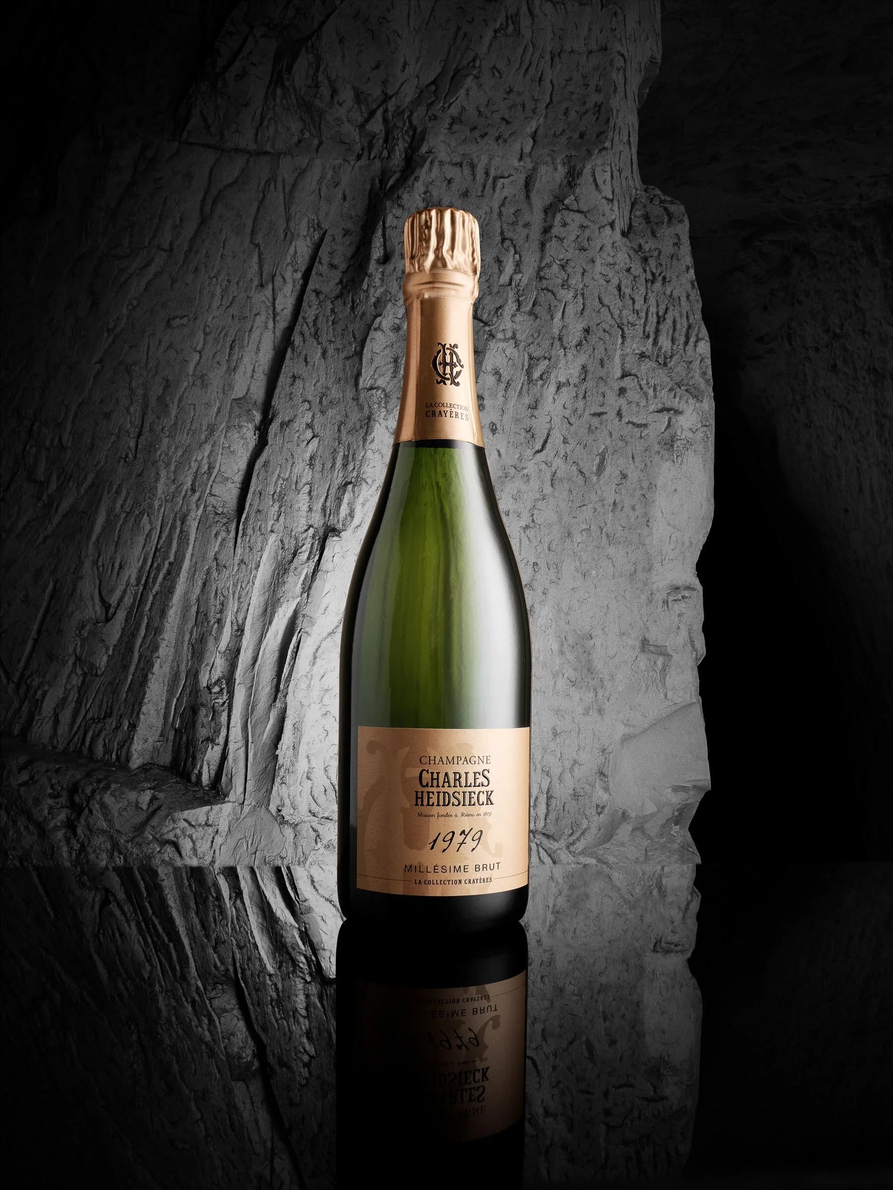 A bottle of 1979 Charles Heidsieck Millesime Brut champagne against a gray rocky background, with a reflection visible below.