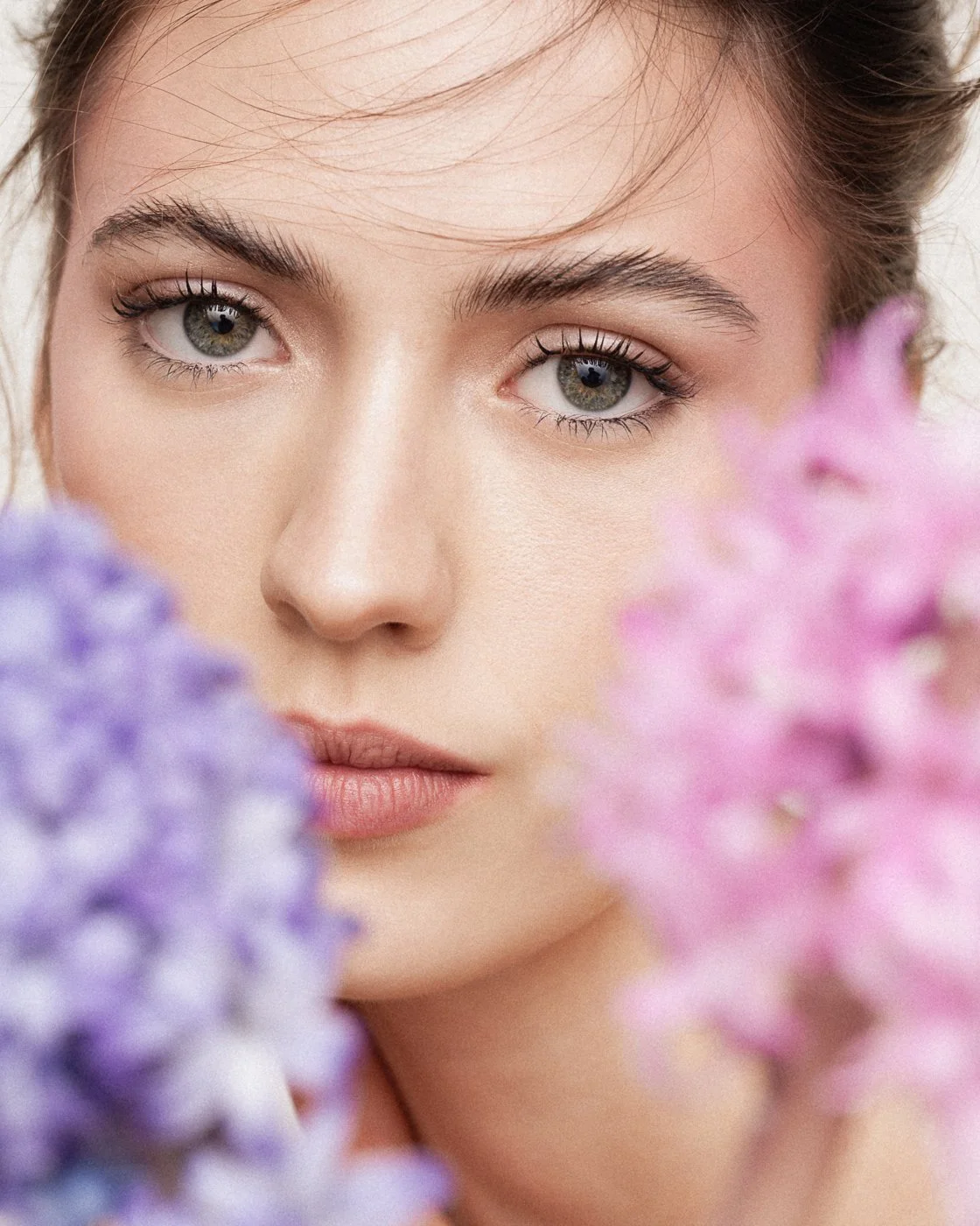 Close-up of a young woman's face with green eyes, surrounded by purple and pink flowers.