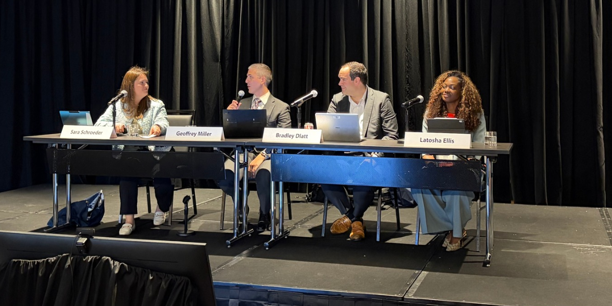 Panelists presenting "AI Governance: Building an AI Use Policy That Works for Your Company" at a table on stage