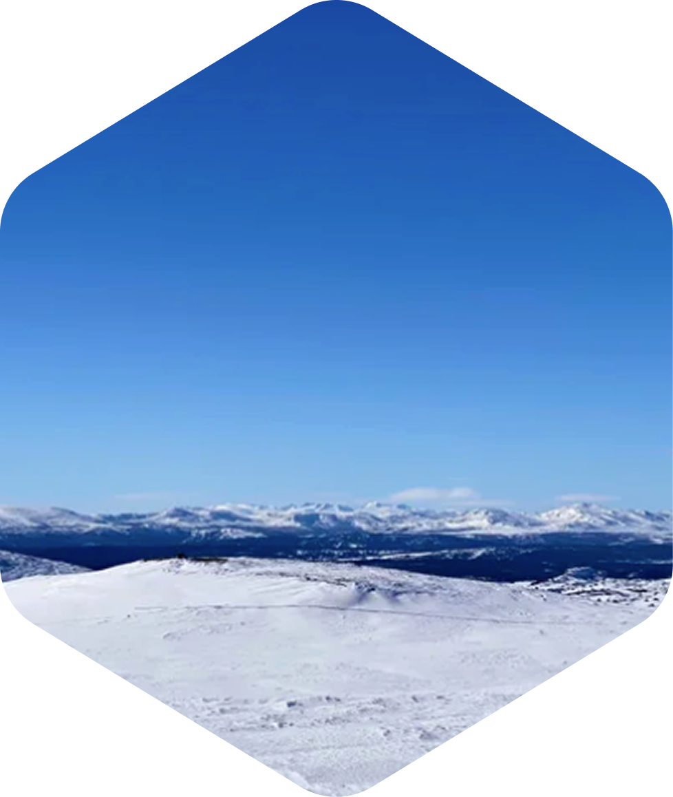 Snødekt fjellandskap under klar blå himmel, med fjell i bakgrunnen.