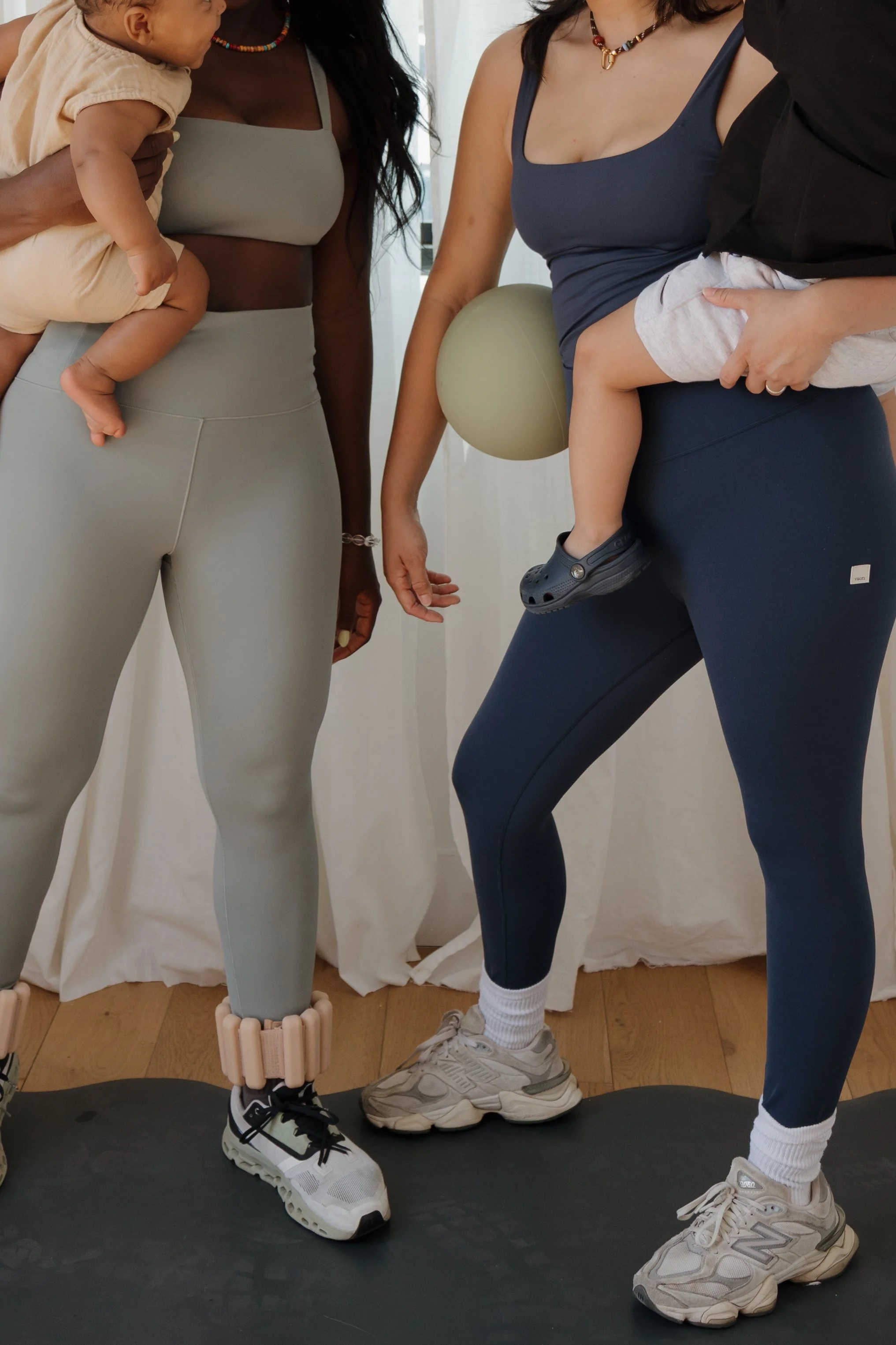 Close-up of two women with children, wearing workout clothes, standing on a treadmill, with balloons in the background.