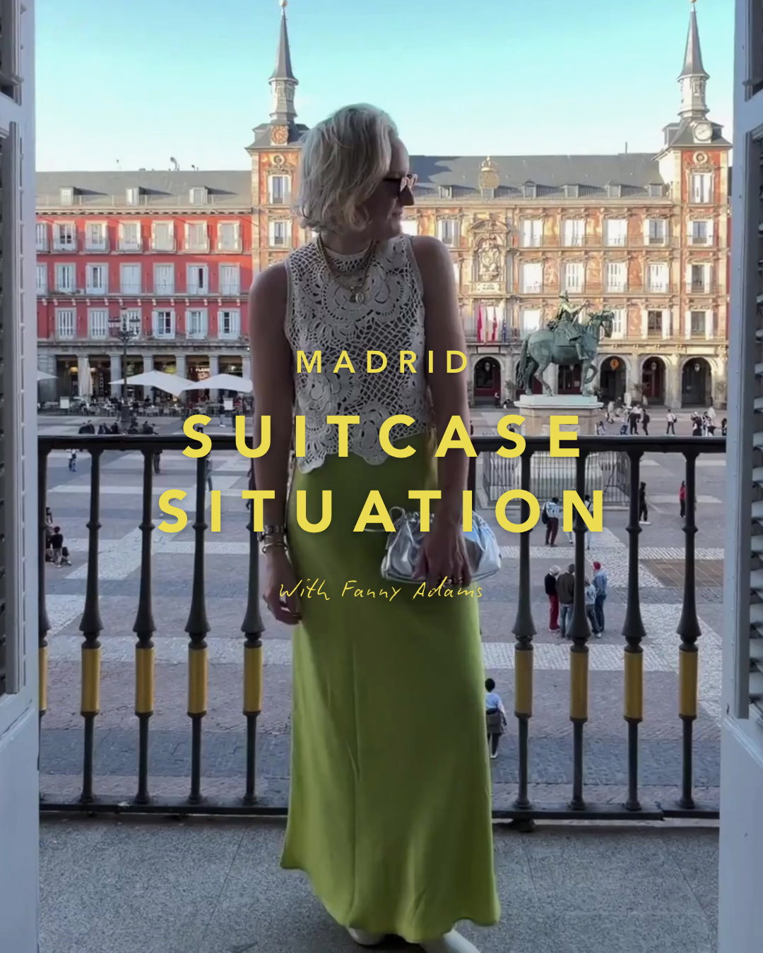 A woman standing on a balcony overlooking Plaza Mayor in Madrid, Spain. She is wearing a white lace top, a long yellow skirt, and sunglasses, holding a purse. The background shows historic buildings and people walking in the square.