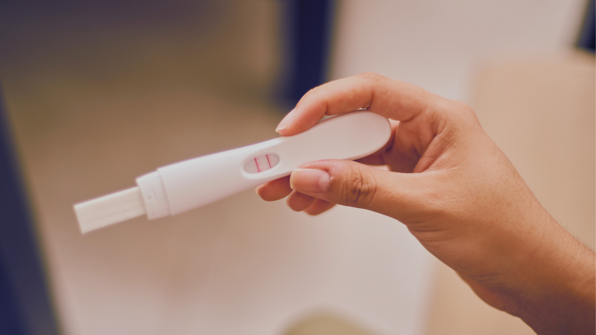 A hand holding a white pregnancy test with two lines