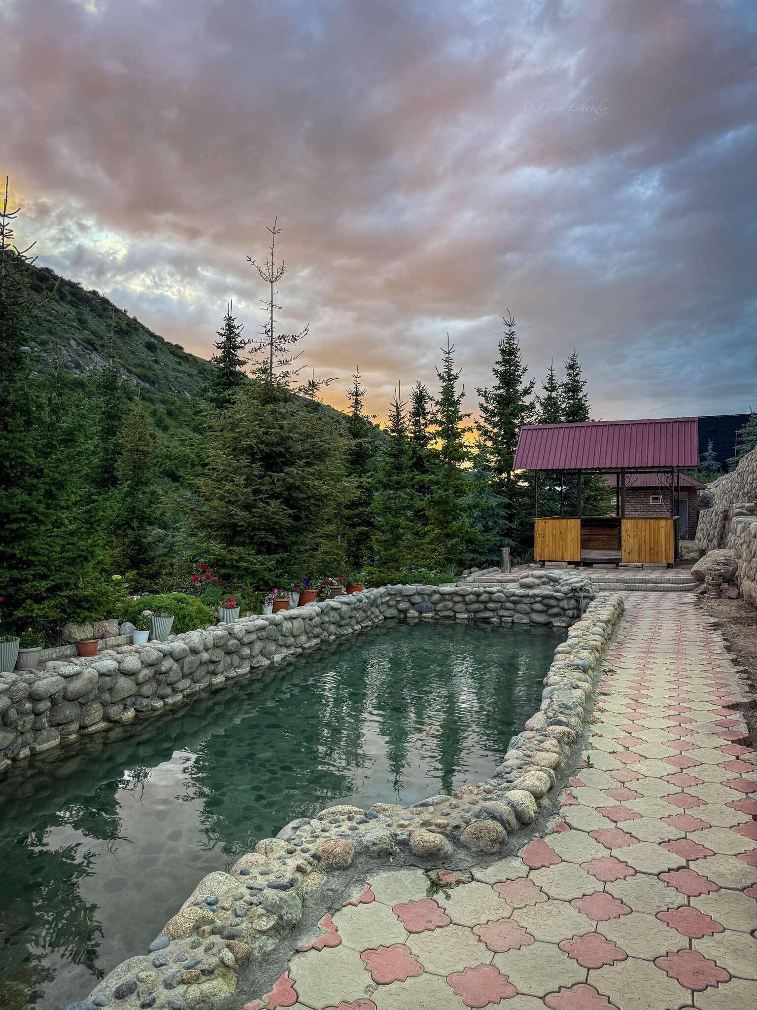 a thermal pool set into the rocks surrounded by green alpine trees in karakol kyrgyzstan