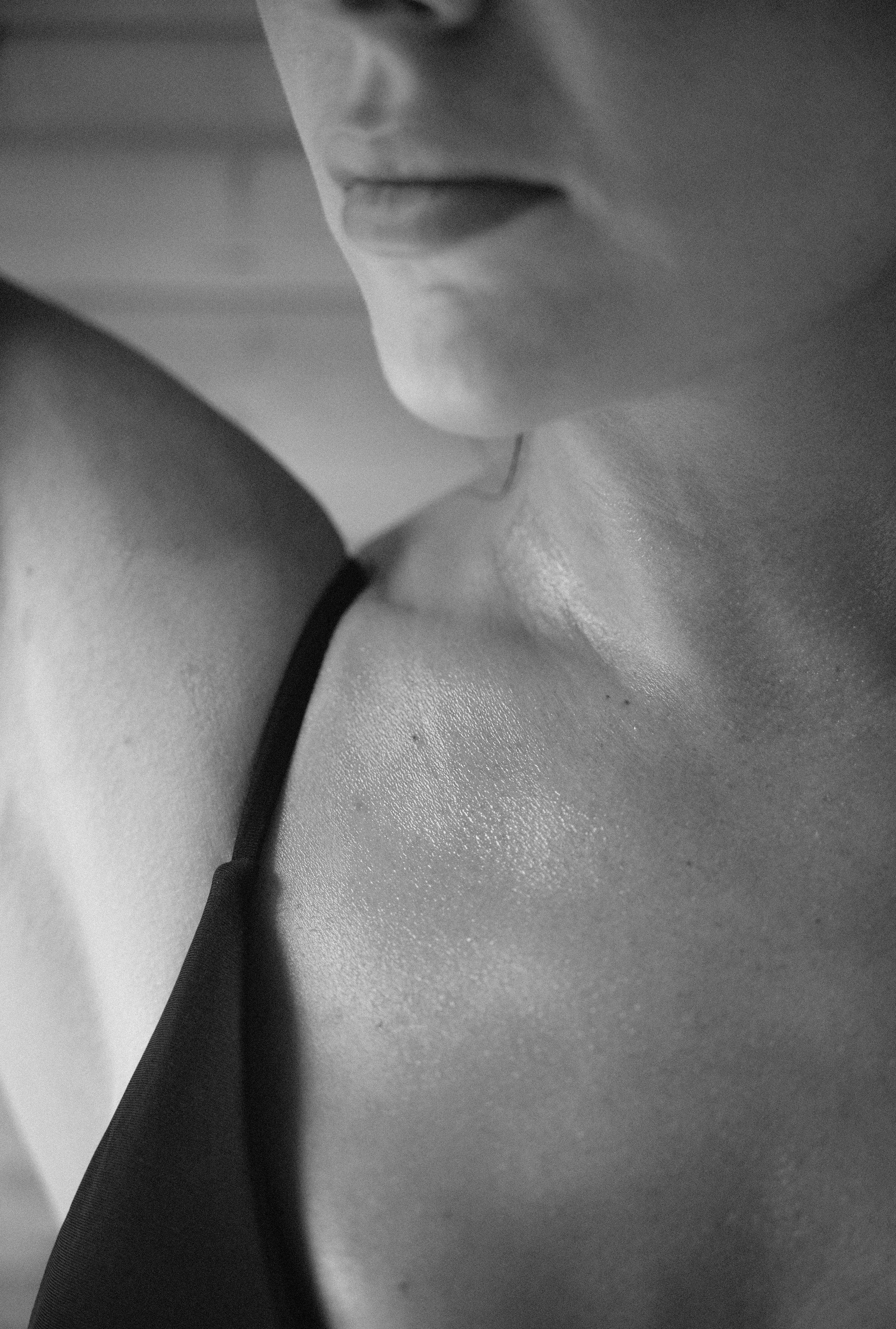 Close-up of a woman's lower face and shoulder in black and white, with part of her neck and a strap of clothing visible.