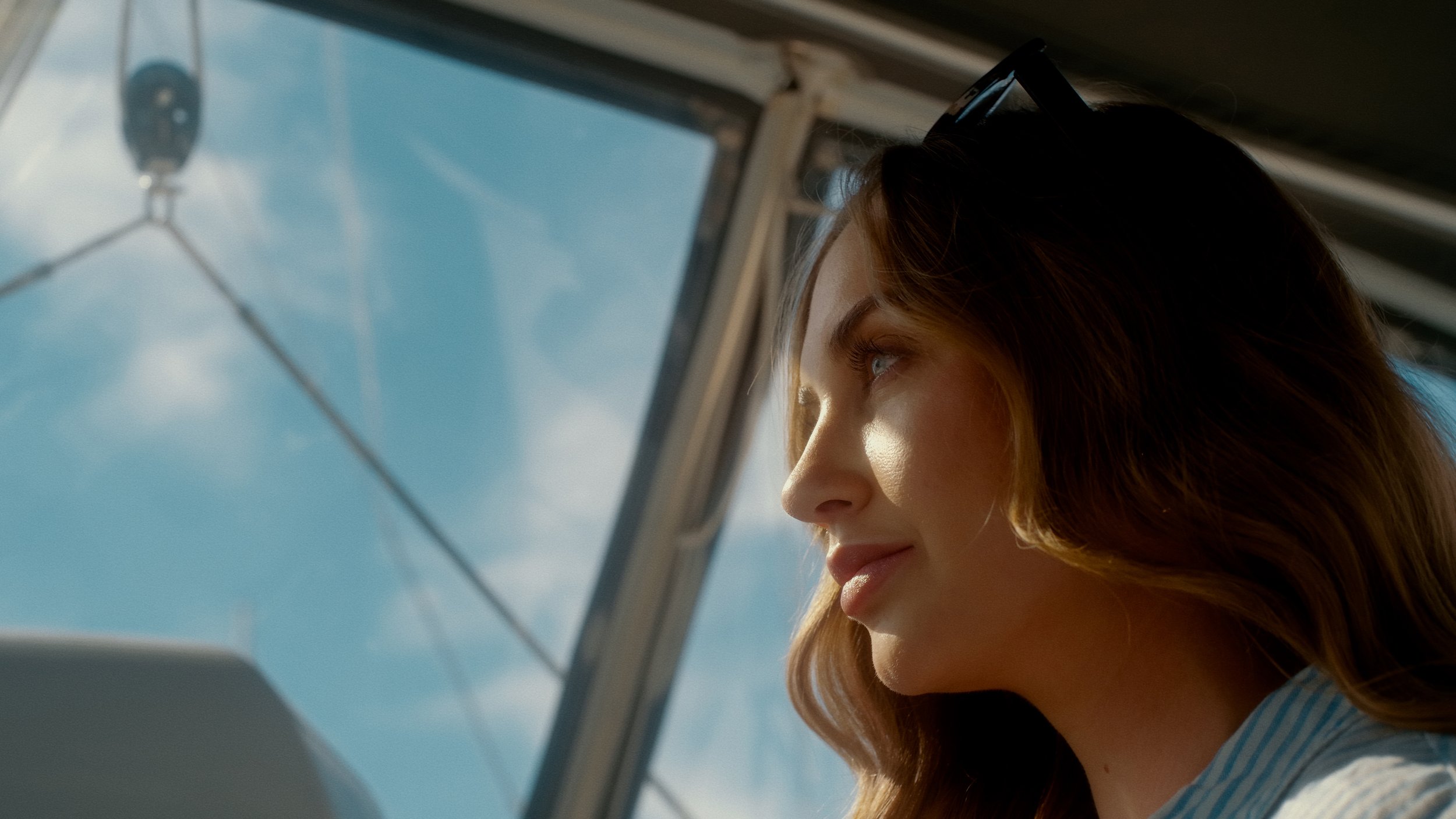 A young woman with brown hair, blue eyes, and freckles looking out of an airplane window at the sky with clouds.