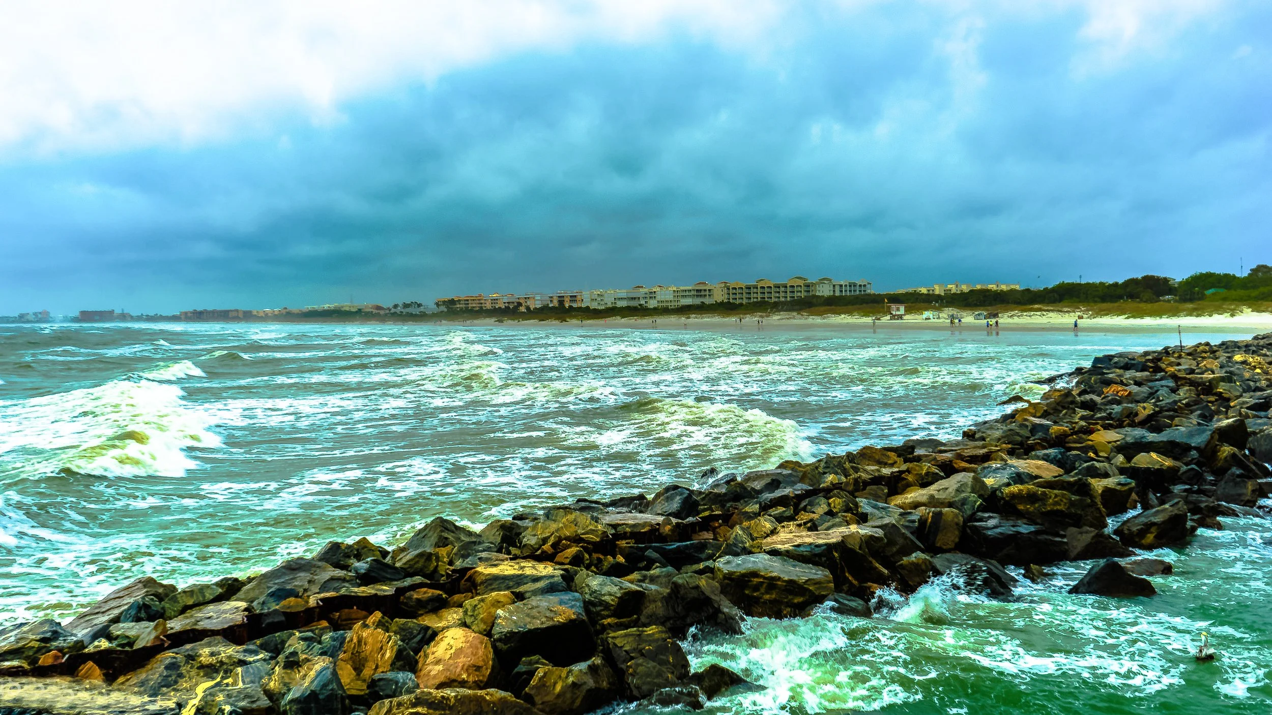 Coastal Vibes limited edition fine art photograph by Jason Sponseller, featuring a rocky Florida shoreline with ocean waves, turquoise water, storm clouds, and distant beachfront buildings