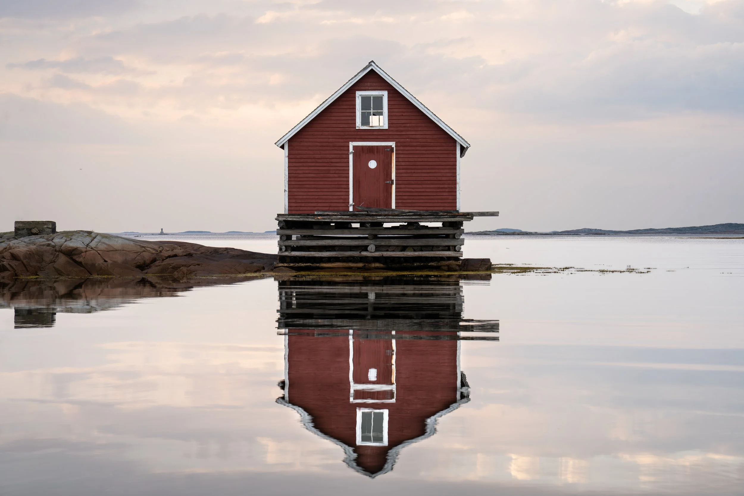 Fine art photograph of a red fishing stage on Fogo Island, Newfoundland, set against calm Atlantic waters and a softly colored morning sky