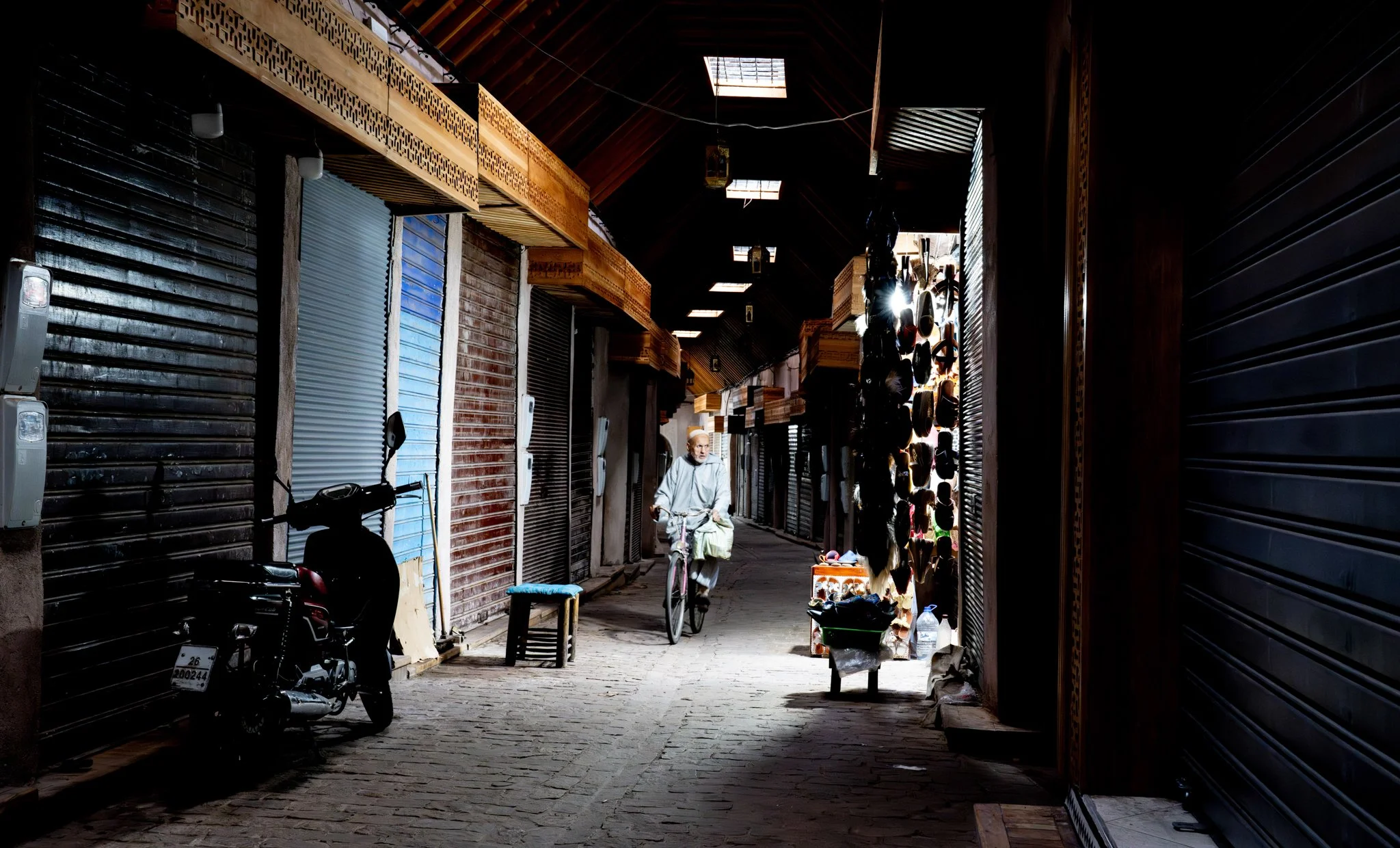 Echo Beneath the Stone, heirloom fine art photograph by Jason Sponseller, featuring a cyclist moving through a dark Moroccan medina passage with old-world architecture, deep shadow, and quiet human presence