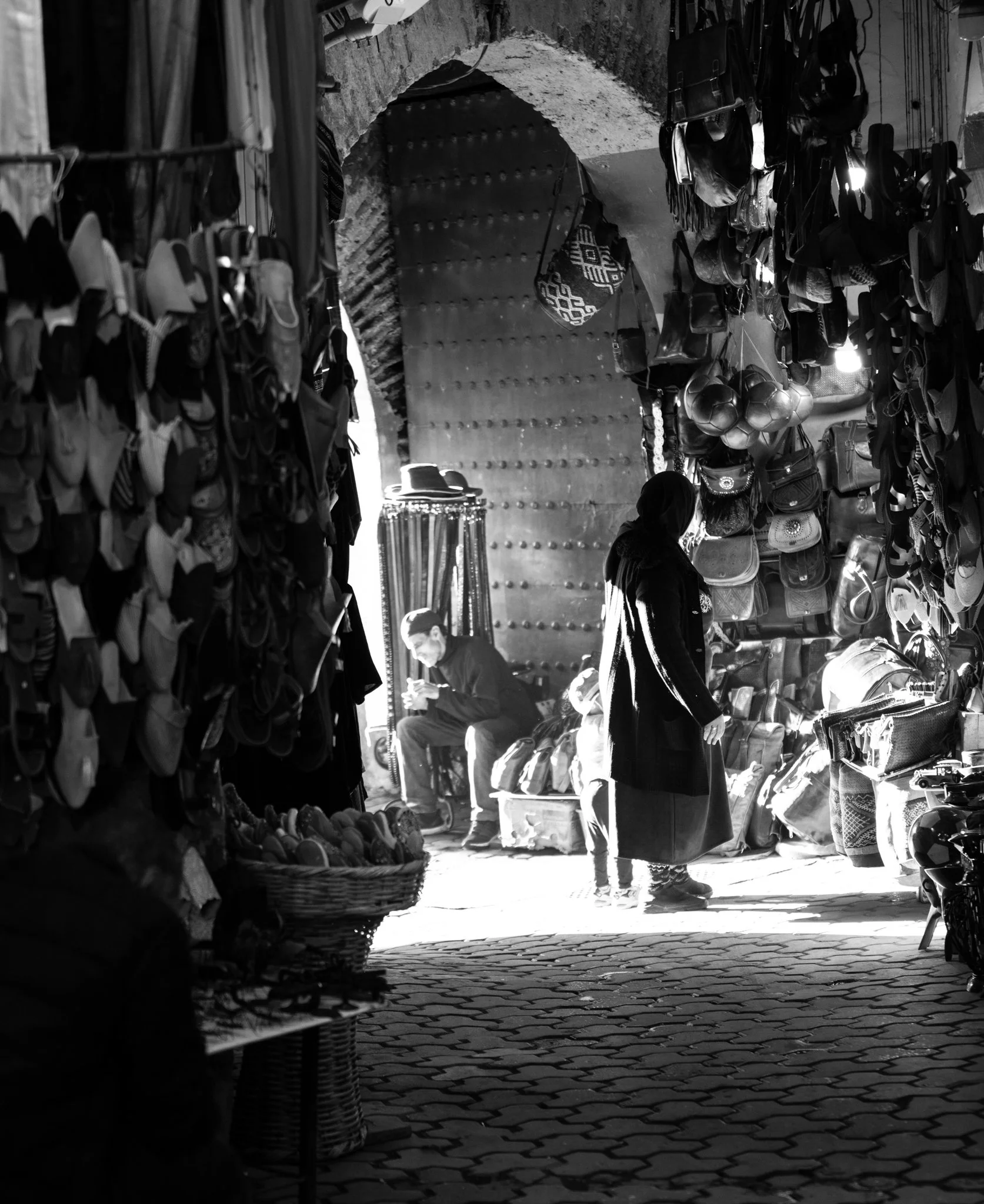 Echo Beneath the Stone, black-and-white fine art photograph by Jason Sponseller, featuring a Moroccan souk passage with historic architecture, layered texture, shadow, and human presence
