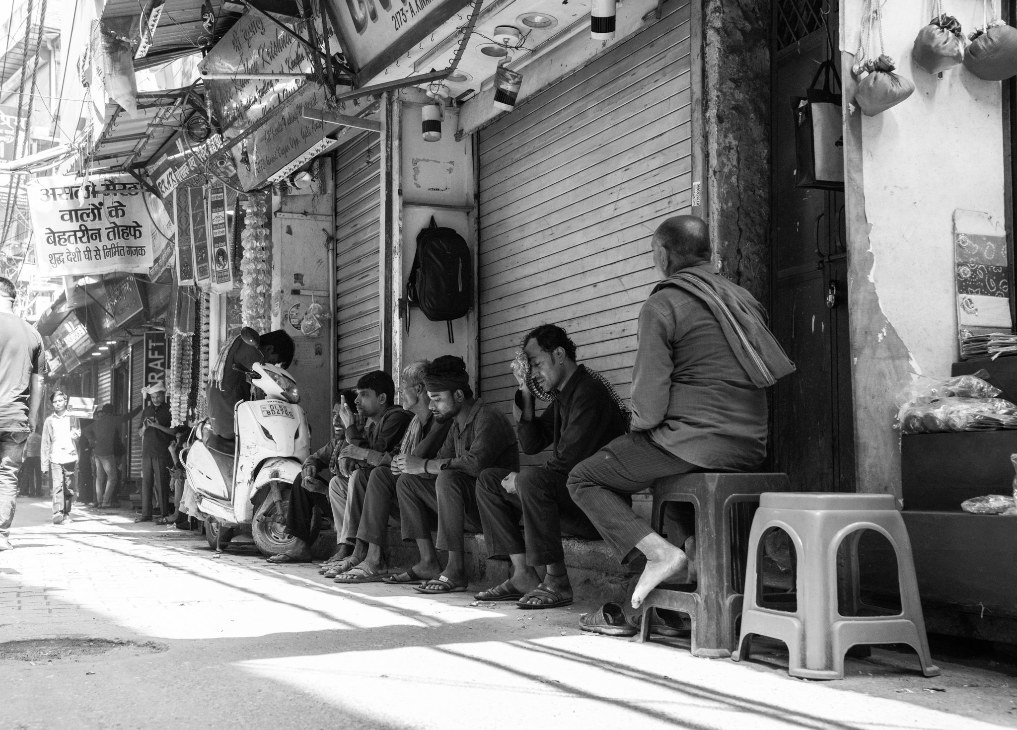 Echo Beneath the Stone, black-and-white fine art photograph by Jason Sponseller, featuring a historic India market street with seated men, old storefront architecture, layered shadow, and human presence