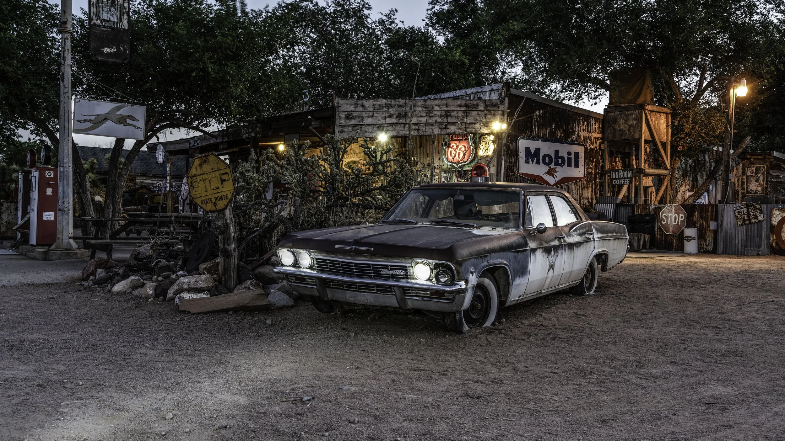 Limited edition fine art photograph by Jason Sponseller, featuring a weathered vintage car outside a Route 66 general store with old gas station signs, neon lights, desert textures, and nostalgic Americana atmosphere