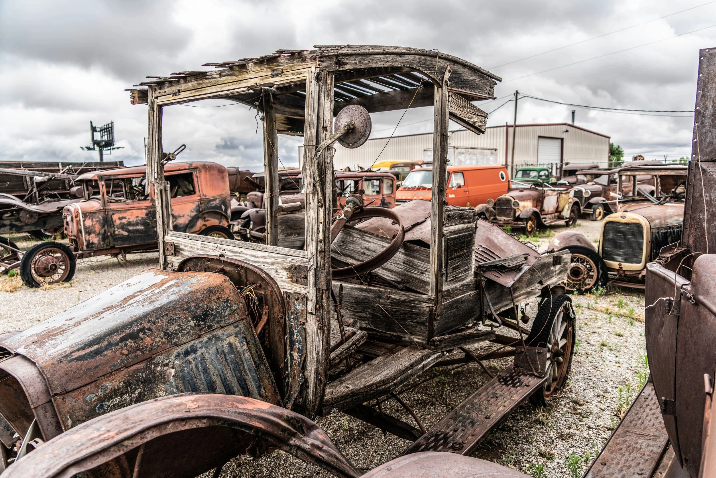 Limited edition fine art photograph by Jason Sponseller, featuring a weathered antique car in a junkyard along Route 66 in Moriarty, New Mexico, with rusted patina, aged wood, vintage automobiles, and nostalgic Americana atmosphere
