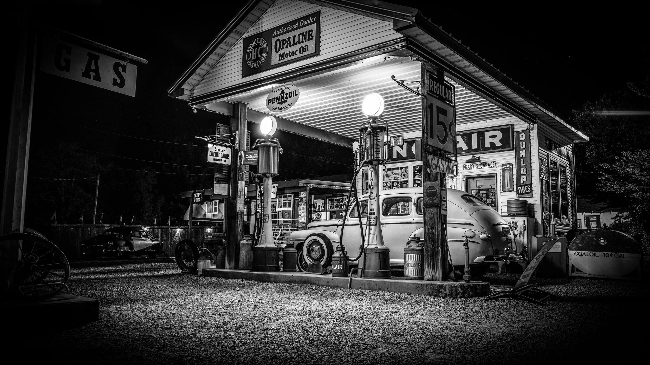 Limited edition black-and-white fine art photograph by Jason Sponseller, featuring Gary’s Gay Parita on Route 66 in Missouri at night with vintage gas pumps, classic cars, glowing lights, and nostalgic Americana atmosphere