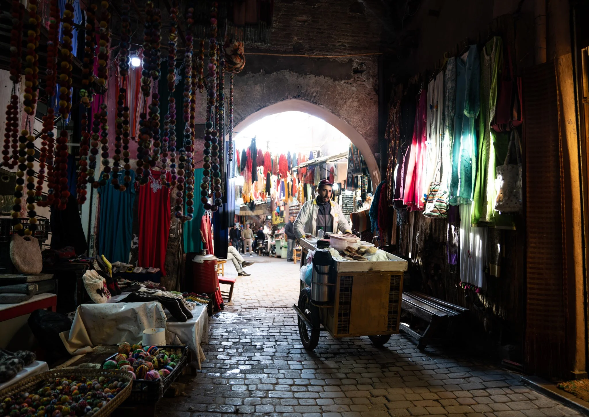 Echo Beneath the Stone, heirloom fine art photograph by Jason Sponseller, featuring a Moroccan souk market passage with rich color, architectural texture, layered shadow, and human presence for curated interiors