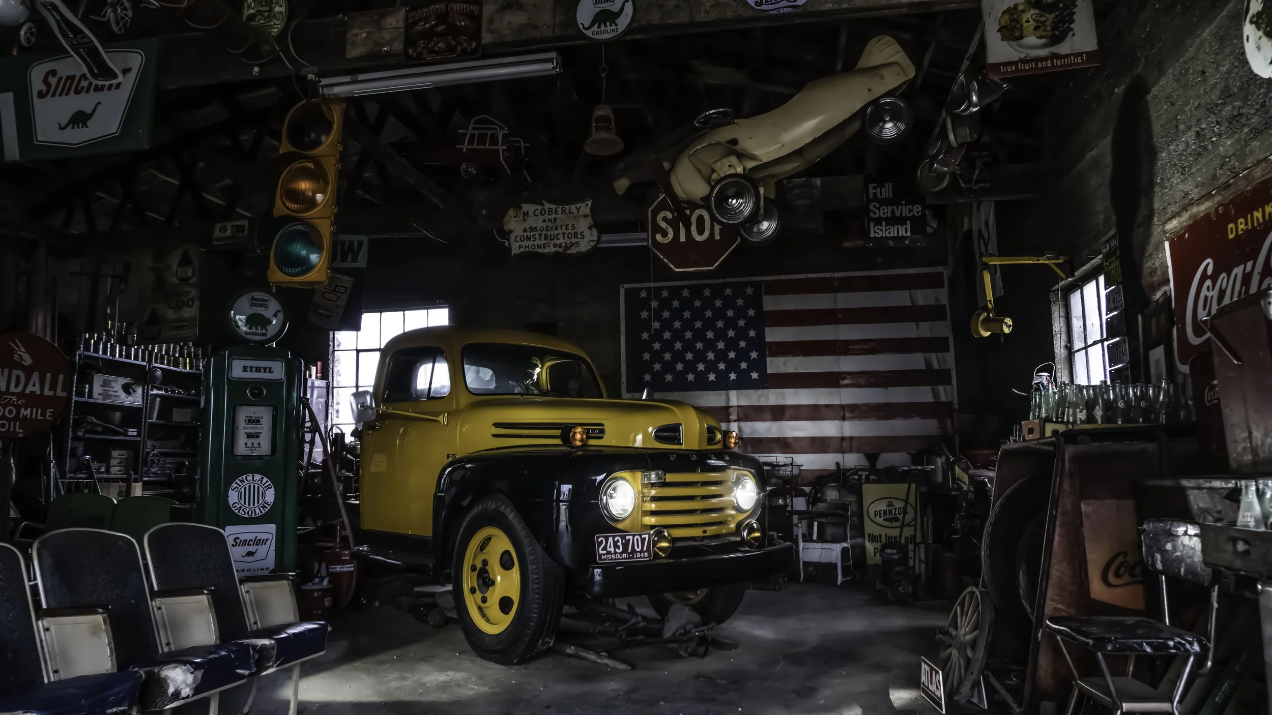 Limited edition fine art photograph by Jason Sponseller, featuring a vintage yellow Ford truck inside an old Americana garage with Sinclair signs, antique gas pumps, American flag, and nostalgic Route 66 atmosphere