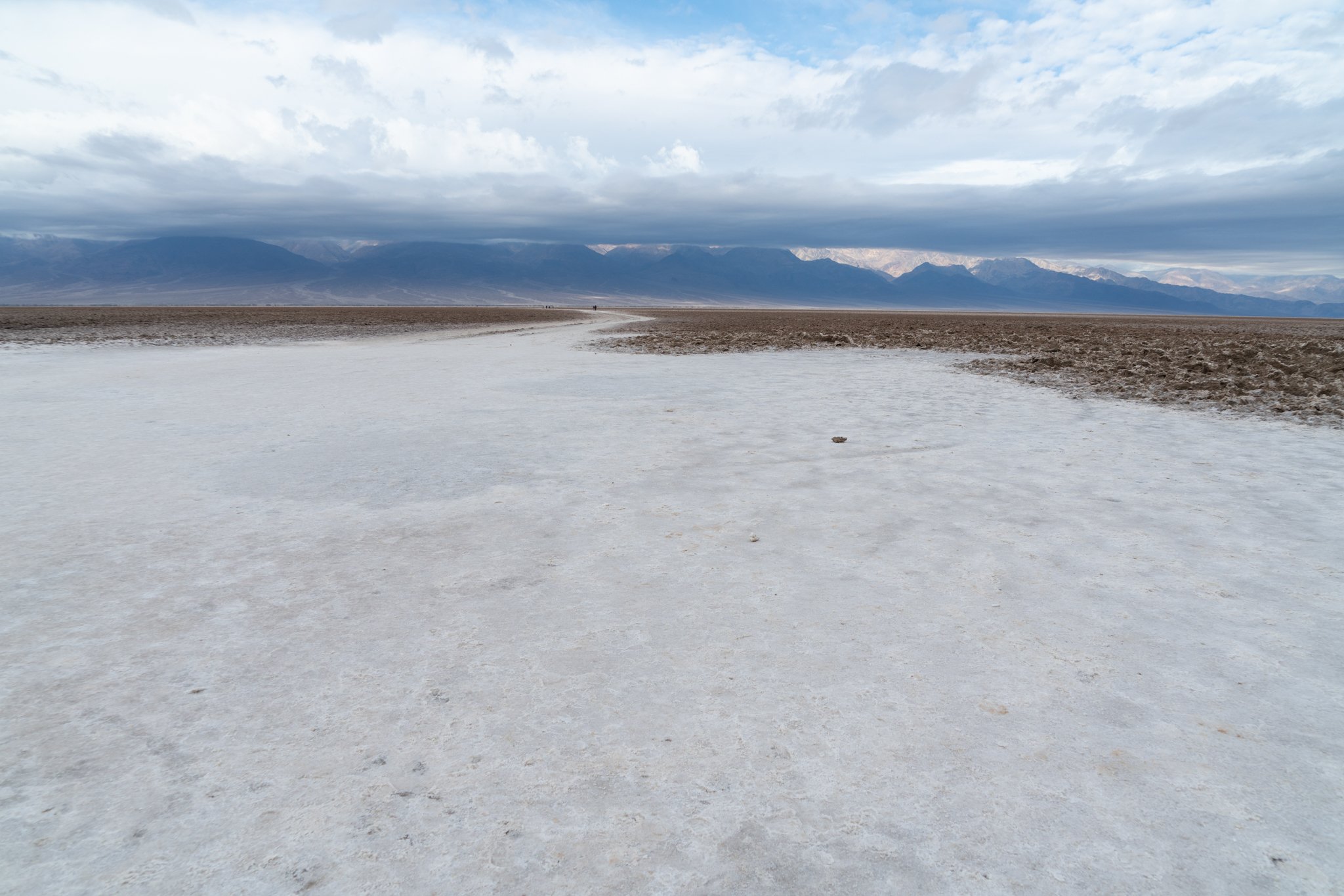 Dust and Distance: The Resonance of Time, limited edition fine art photograph by Jason Sponseller, featuring a vast salt flat in Death Valley leading toward distant mountains beneath heavy clouds, with silence, scale, and open desert atmosphere