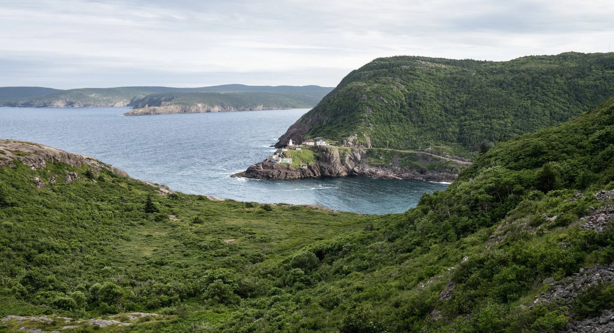 Fort Amherst Lighthouse with rugged coastal cliffs and, green hills, Atlantic water, and quiet atmospheric distance