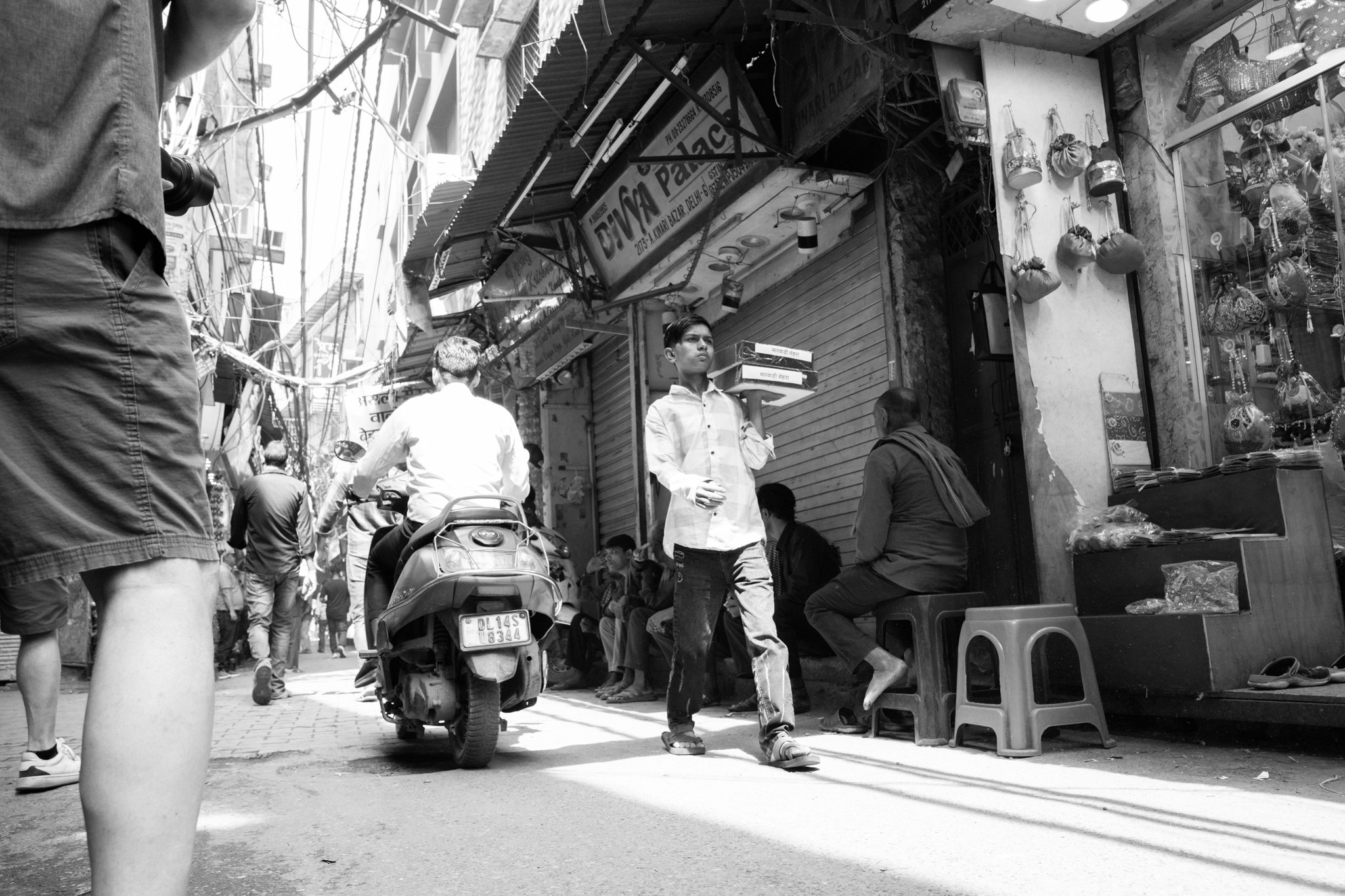 Echo Beneath the Stone, black-and-white documentary fine art photograph by Jason Sponseller, featuring Kinari Bazaar in Delhi with a busy market street, old storefronts, overhead wires, and human presence